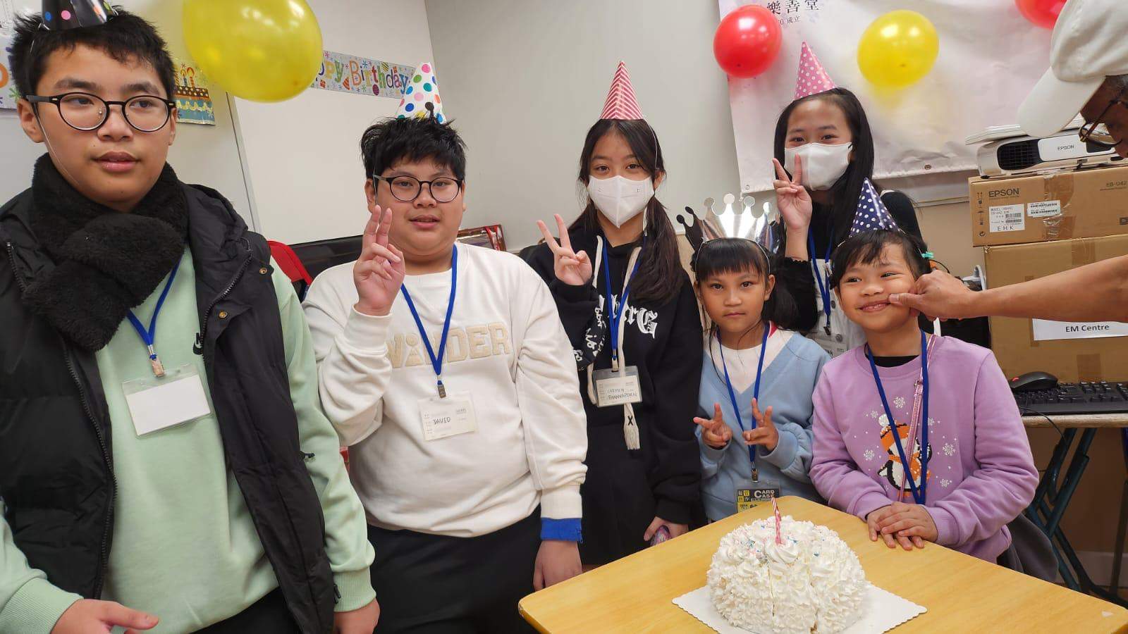 Adults and children gather behind a cake with candles.