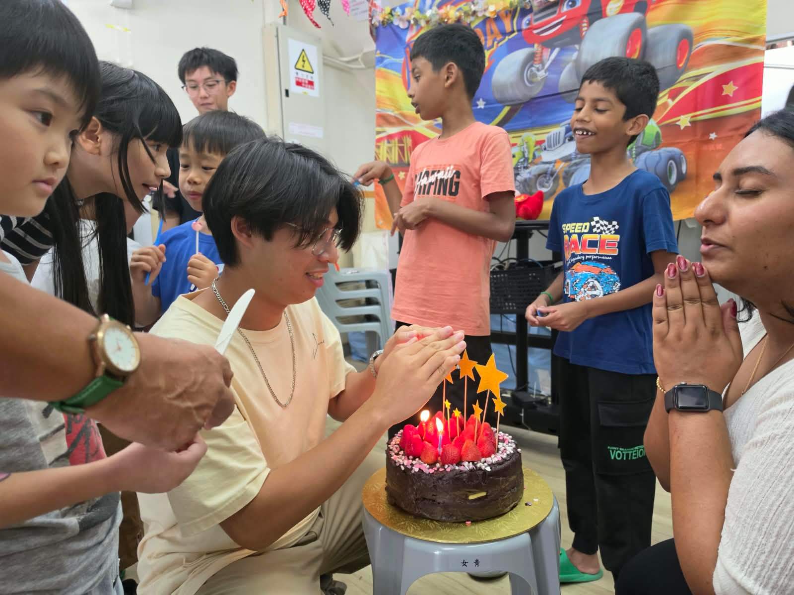 Children and volunteers gather around the lit birthday cake.