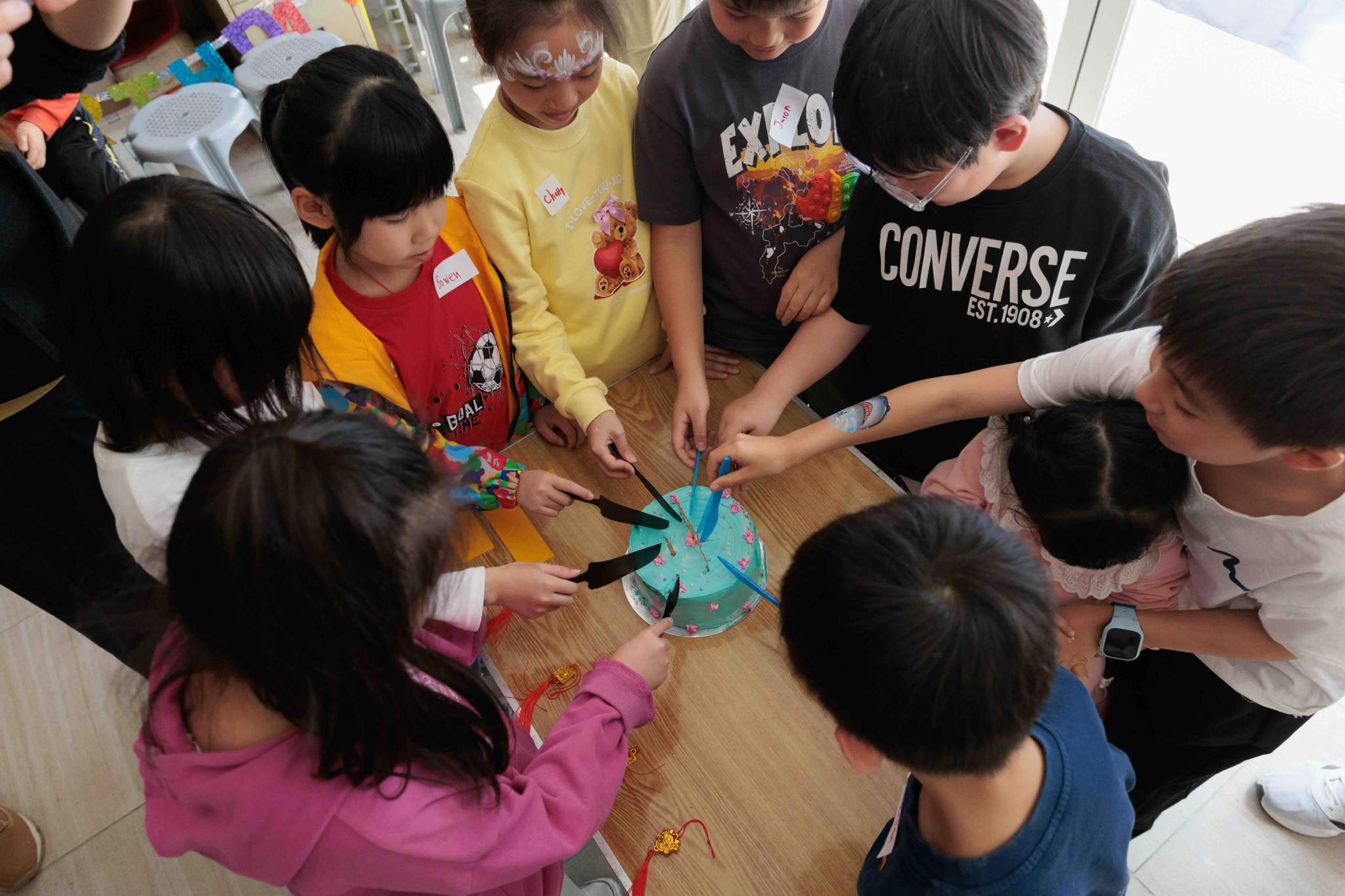 Children gather around a table while cutting a blue cake.