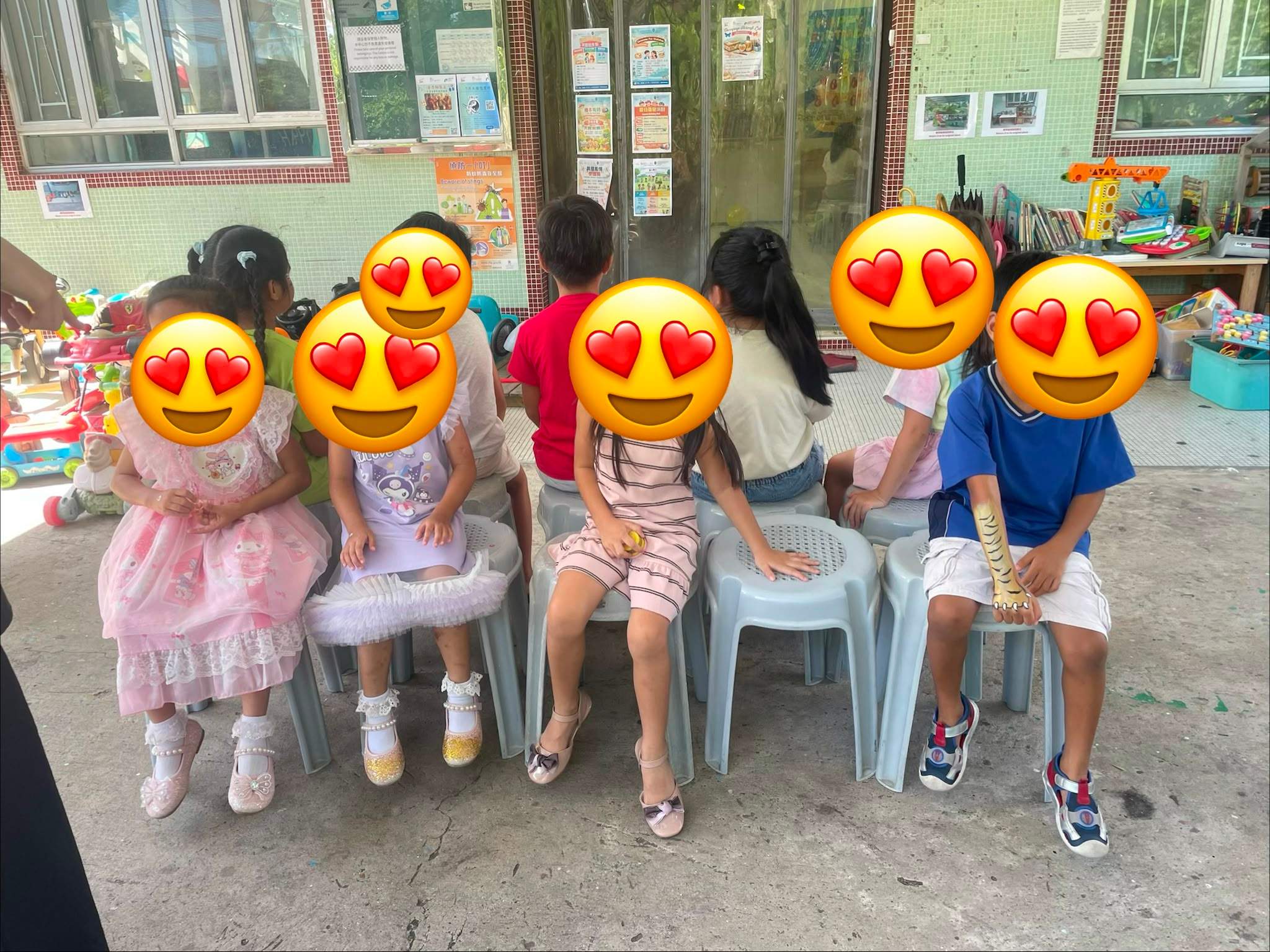 Children sit in a row while adults stand behind them.