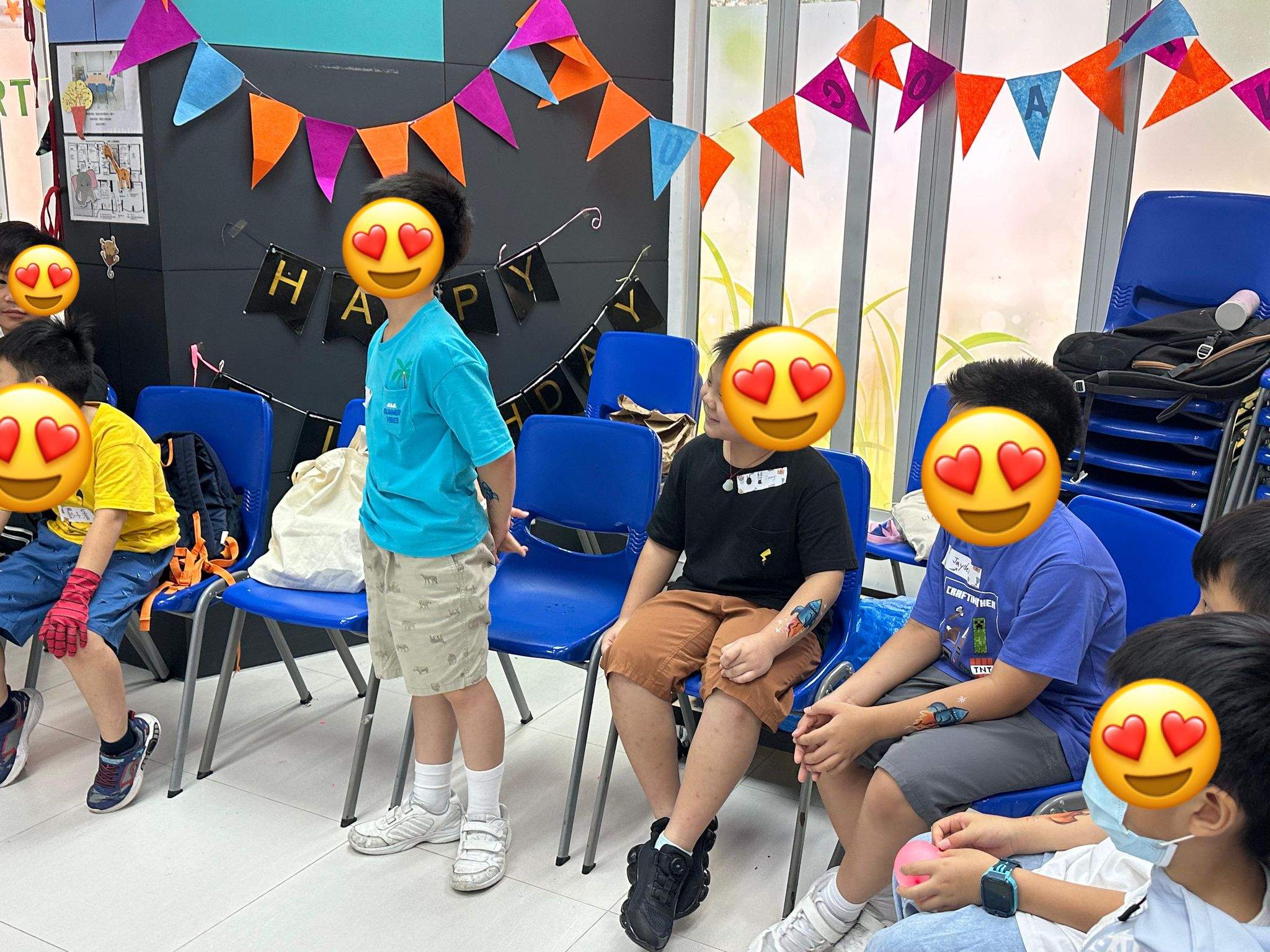 Children sit on blue chairs beneath colourful bunting.