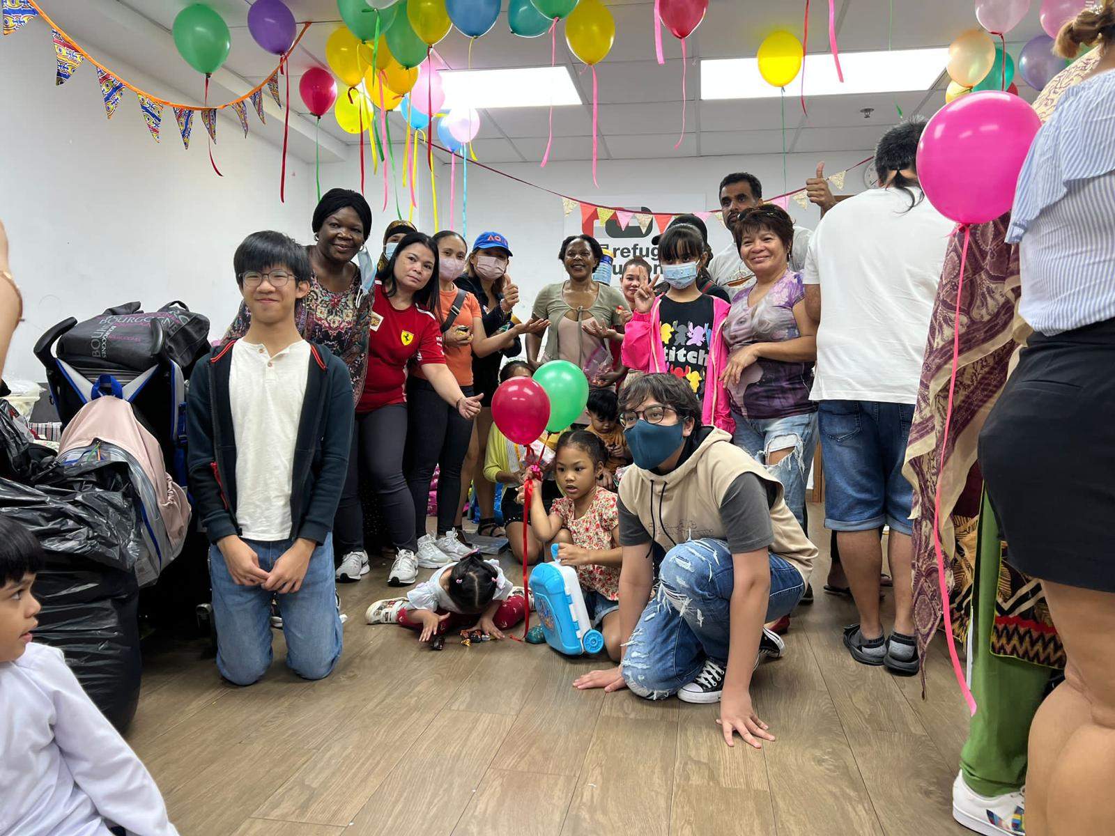 A large group poses together beneath colourful balloons and hanging ribbons.