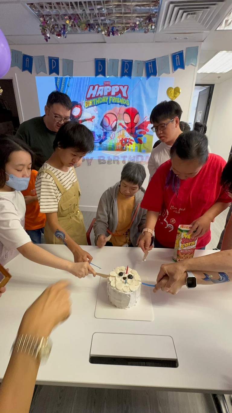 Several people lean over a table while cutting a cake.