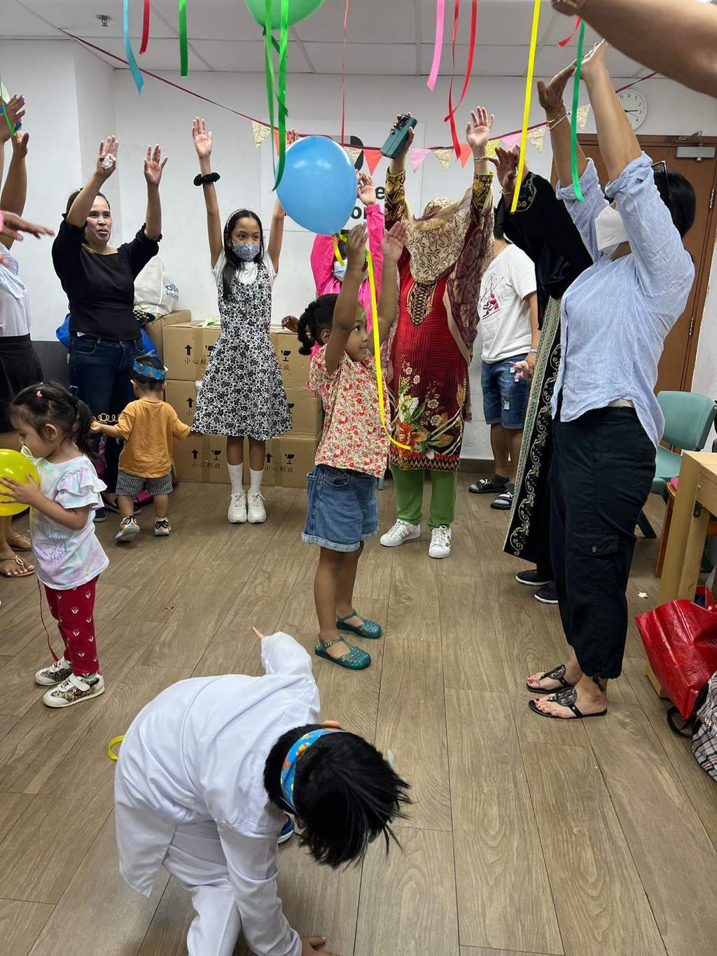 People reach towards hanging ribbons while a child crouches below.
