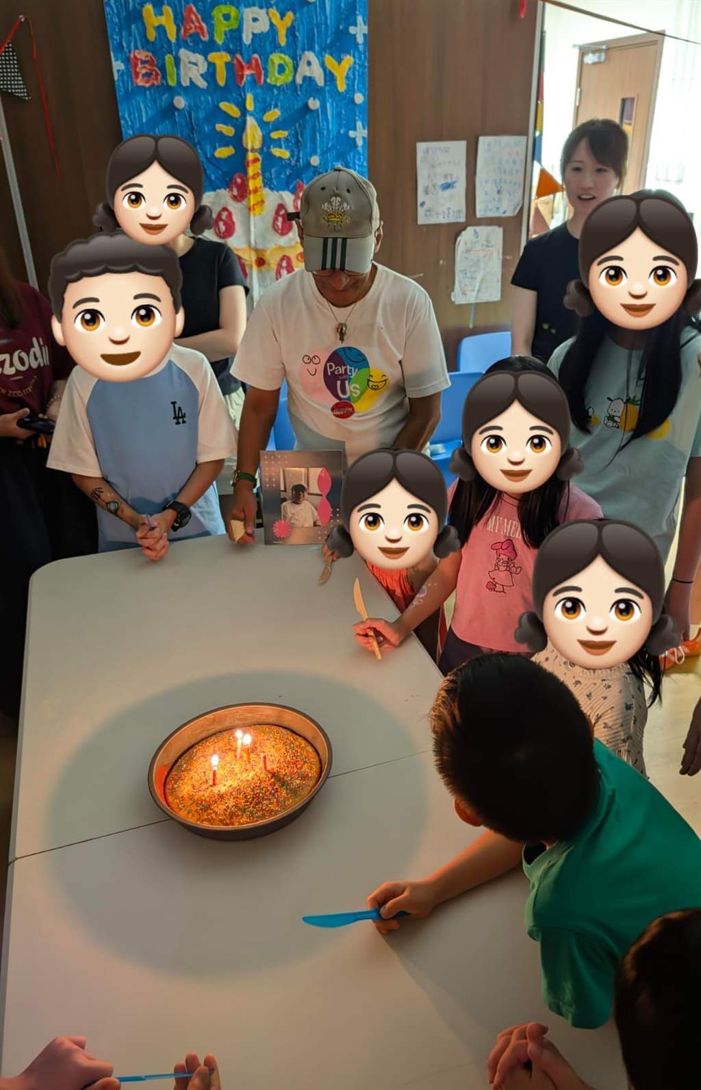 Children and volunteers gather around a birthday cake with lit candles.