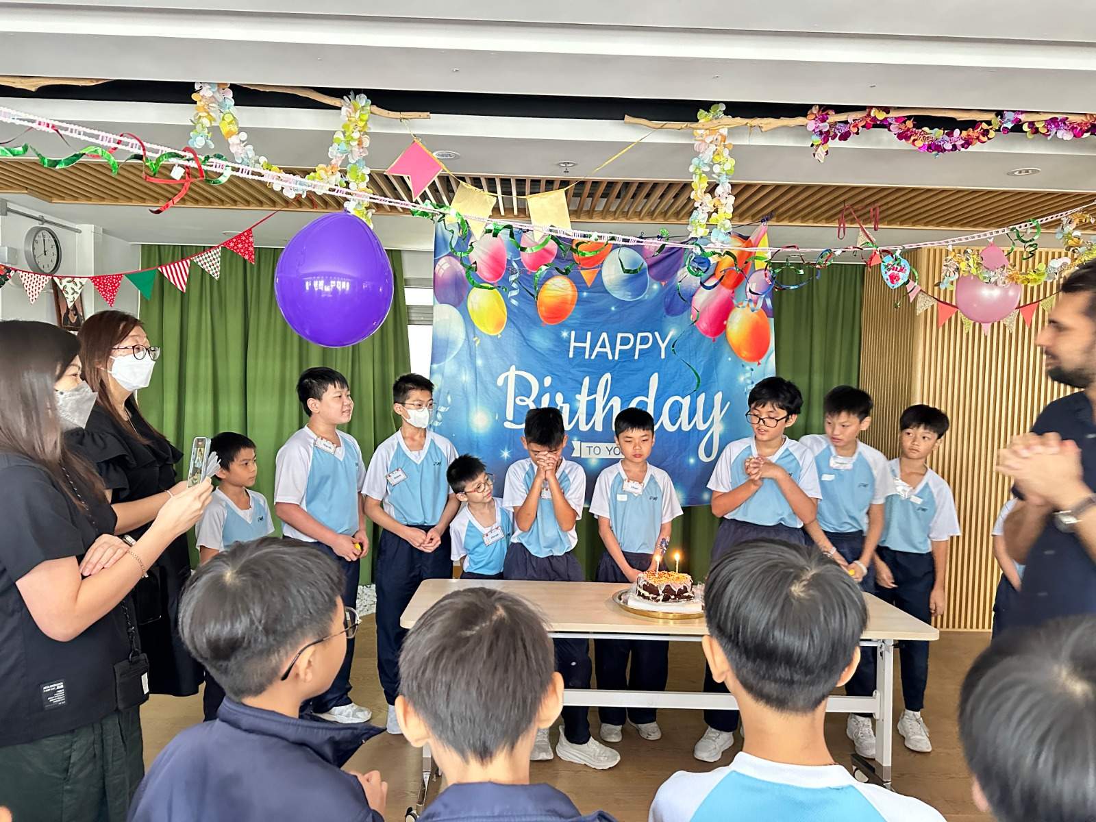 Children gather around a cake table while adults stand nearby.
