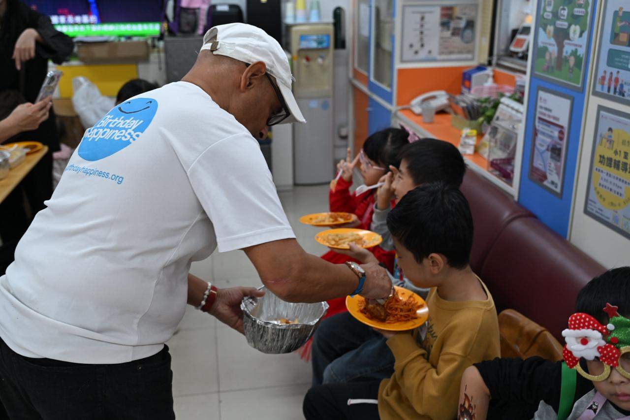 An adult serves food onto plates for seated children.