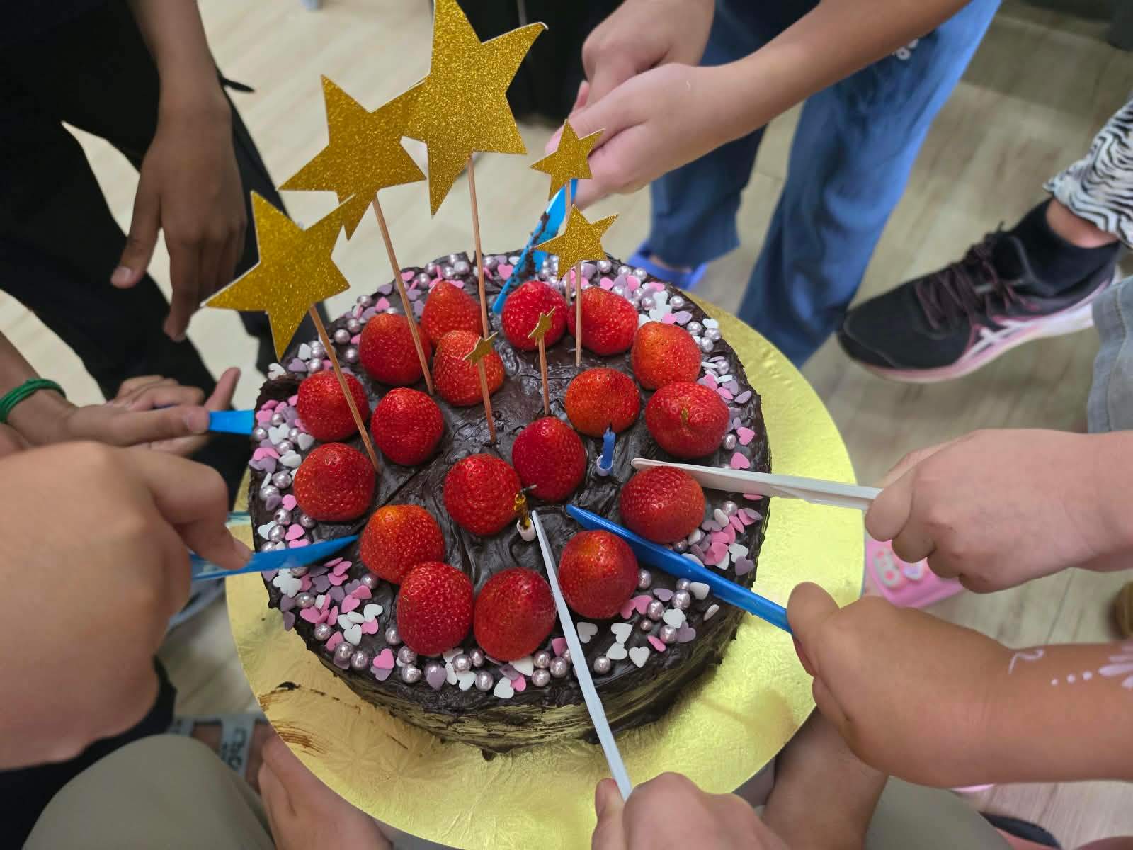 Children gather around a strawberry-topped birthday cake.
