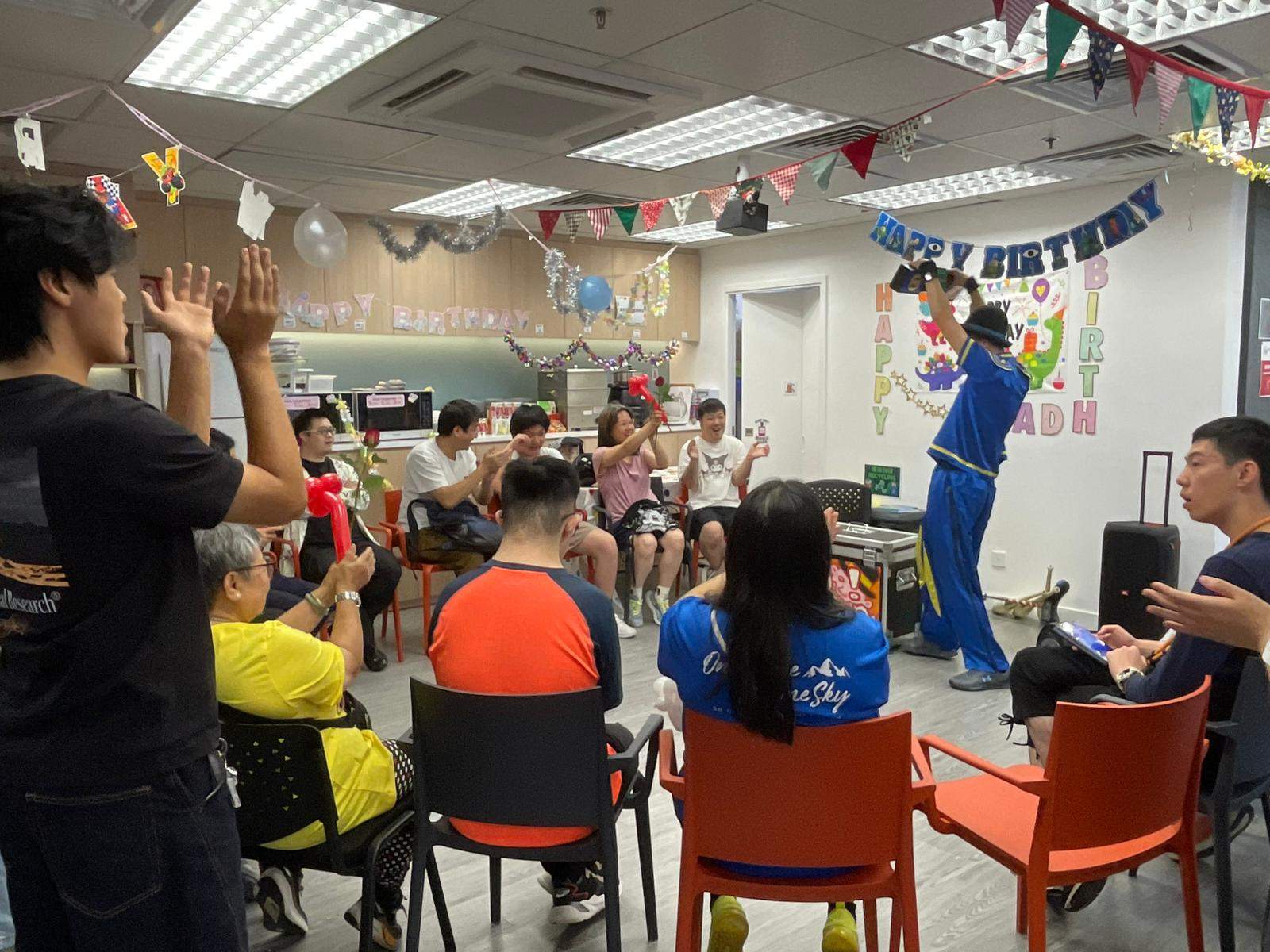 A seated audience watches a performer beneath hanging decorations.