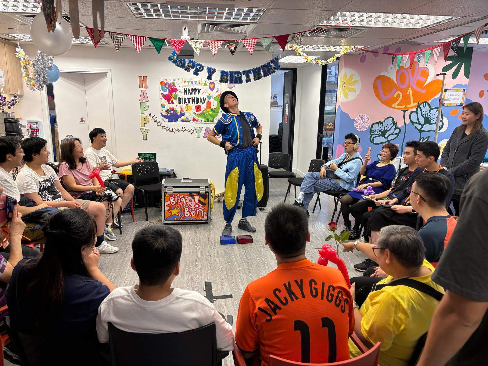 A performer addresses a seated group in a decorated room.