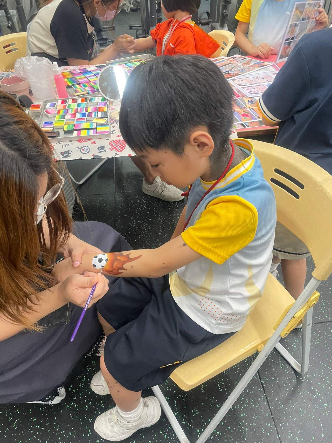 An adult paints a seated child's forearm at a table.
