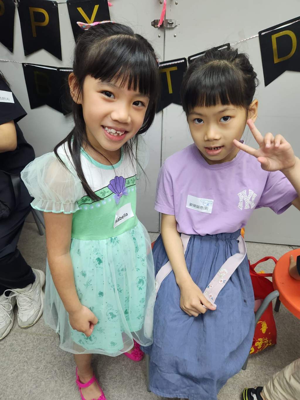 Two children stand together in front of birthday decorations.