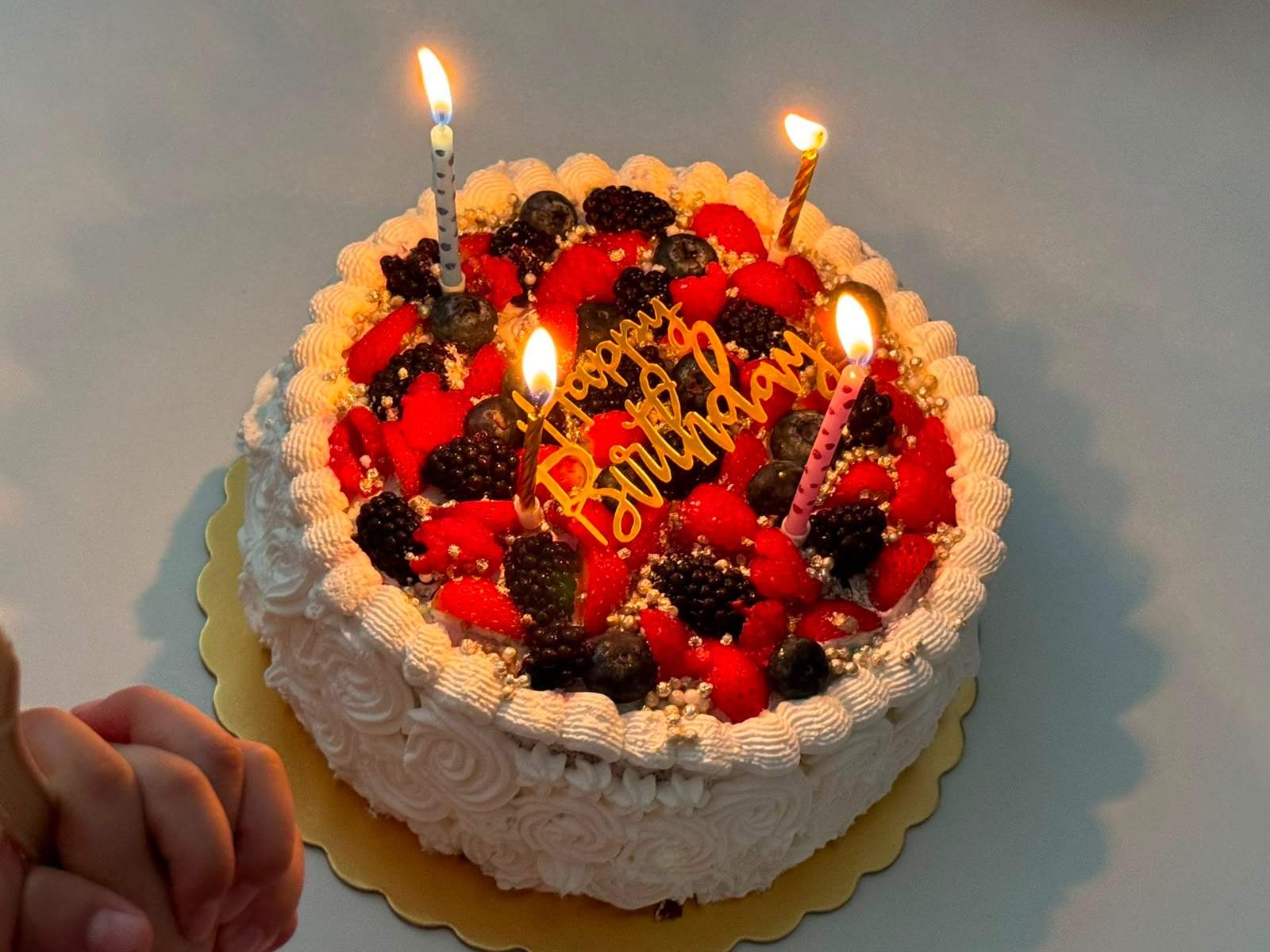 A berry-topped birthday cake is displayed with lit candles.