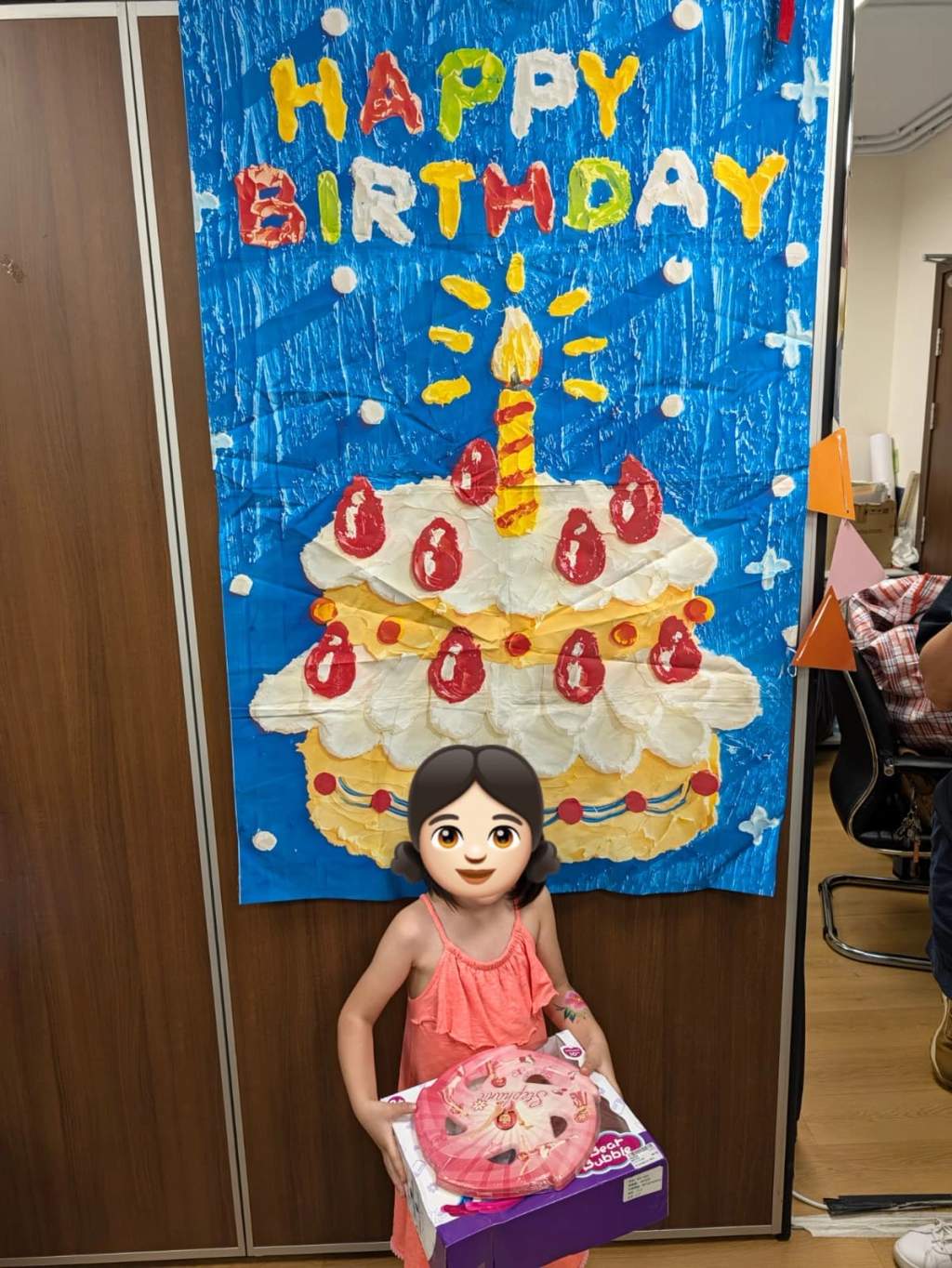 A child displays party gifts in front of the birthday backdrop.