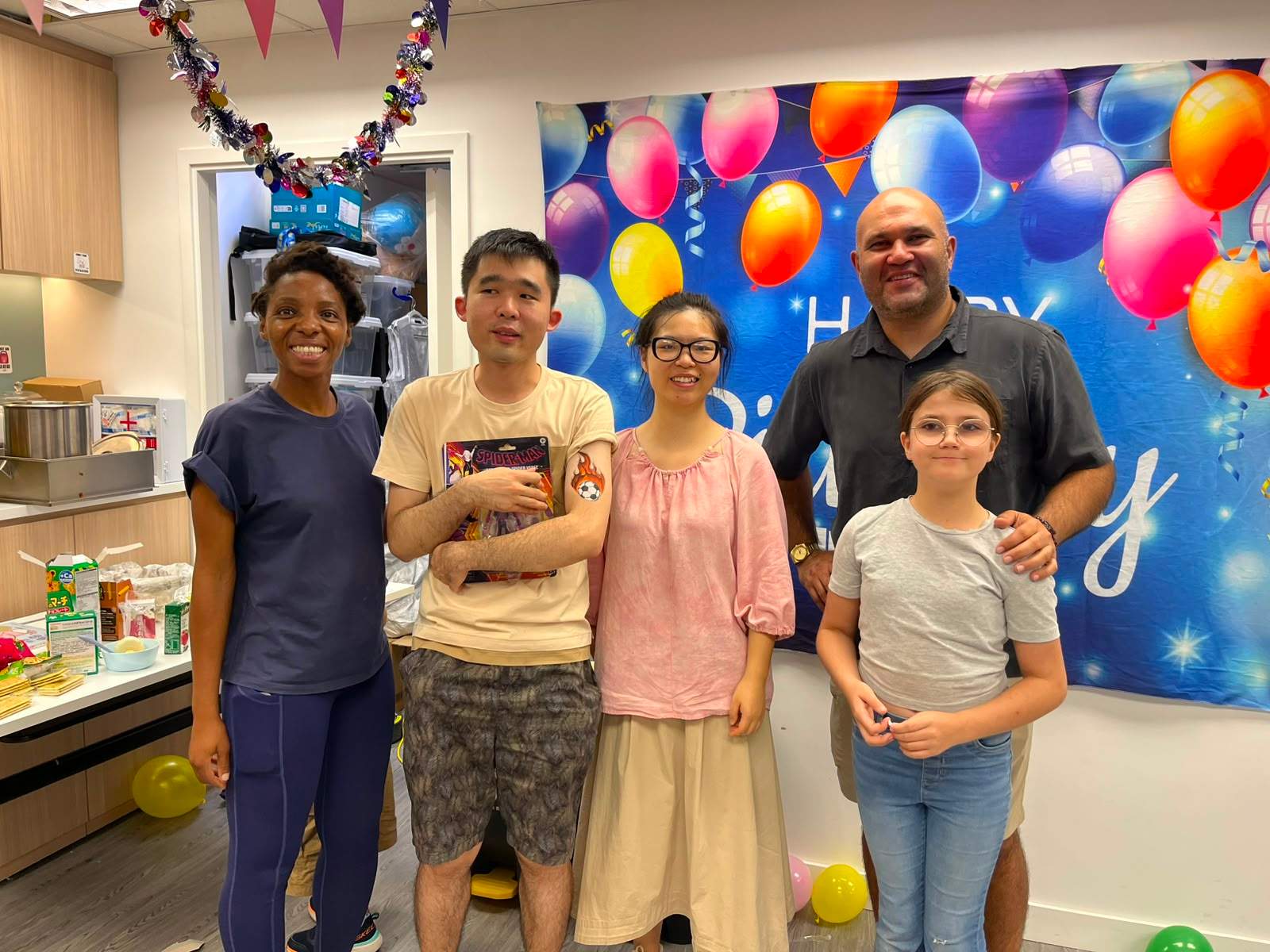 Five people pose together beside a birthday backdrop.