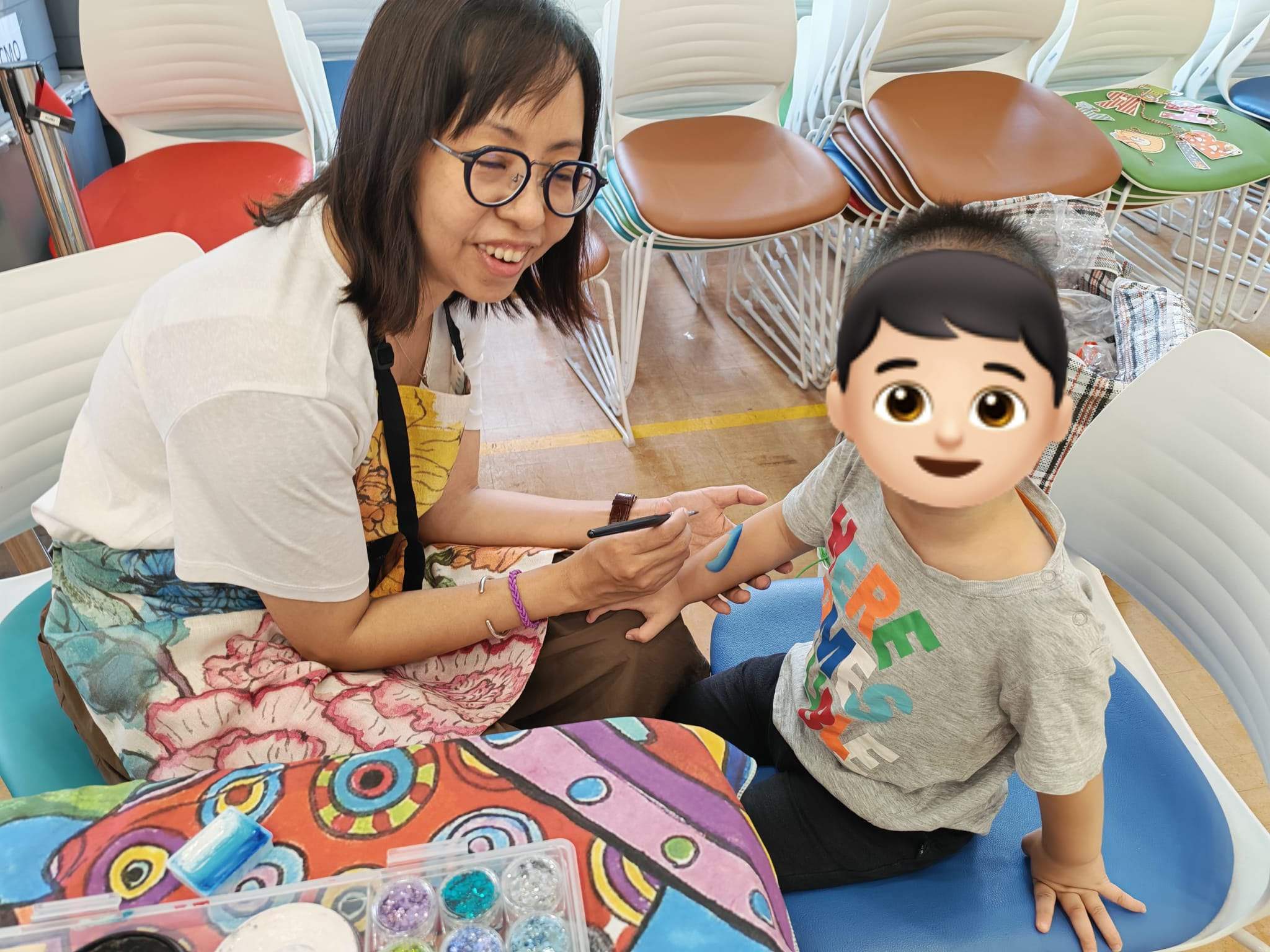 An adult applies face paint to a seated child.