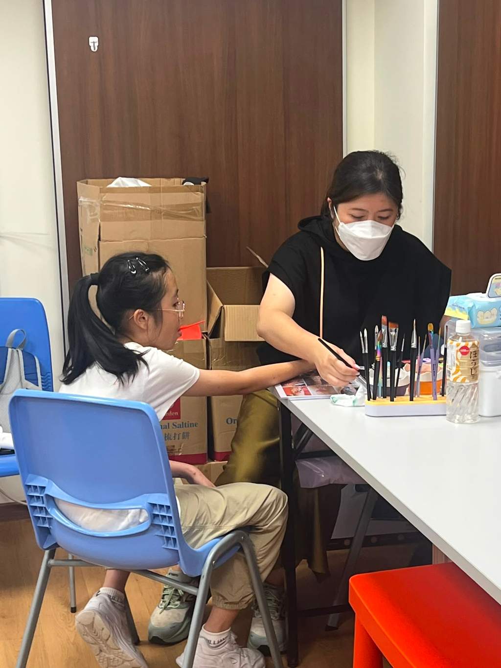 An adult applies face paint to a seated child.