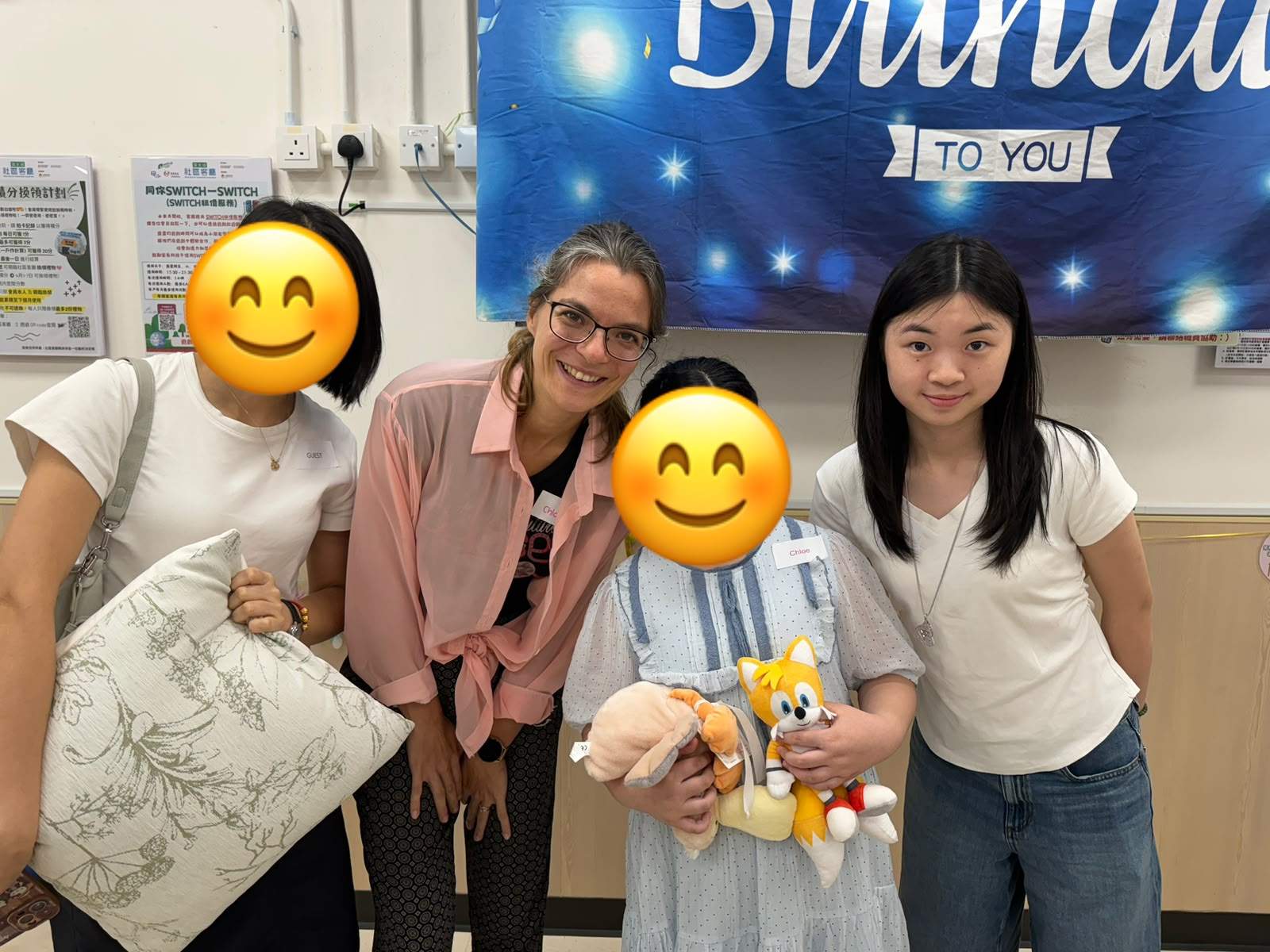 Three adults pose with two children holding stuffed toys.