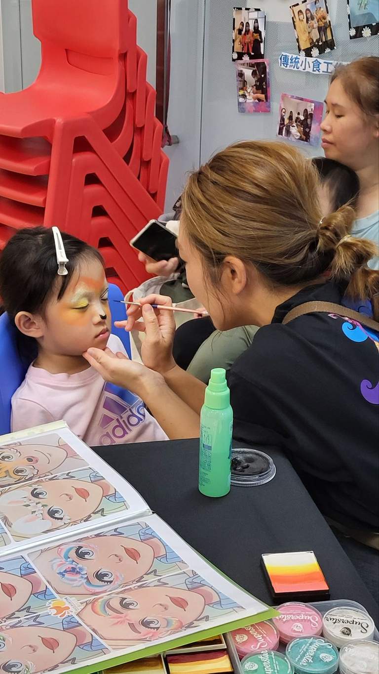 An adult paints a seated child's face at a table.