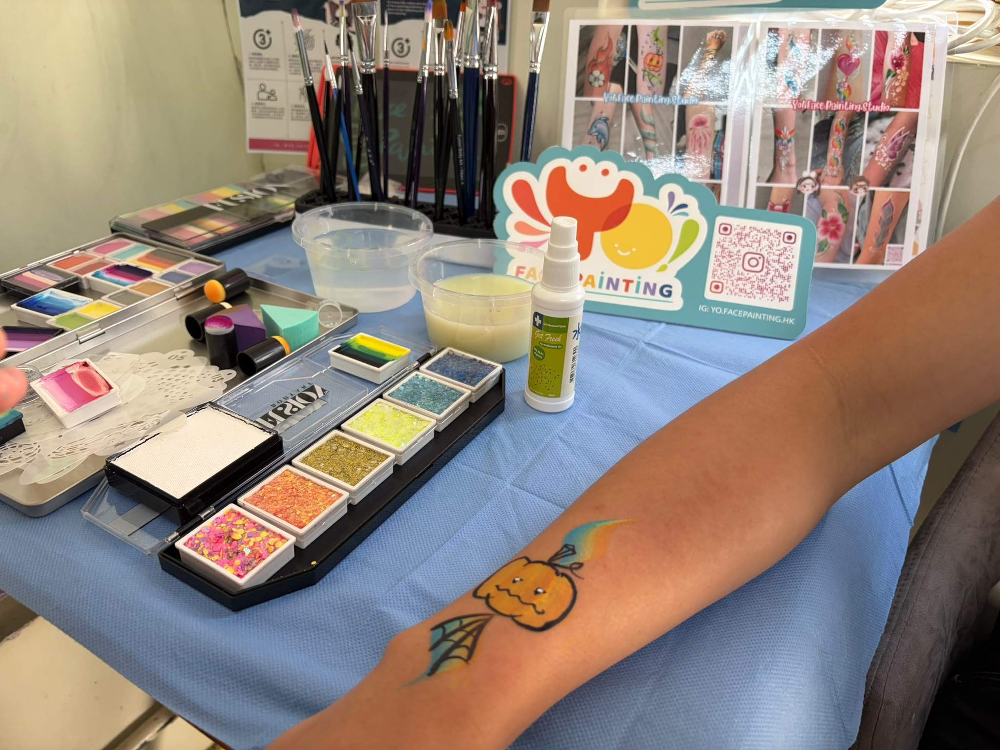A painted pumpkin design is displayed beside face-painting supplies.