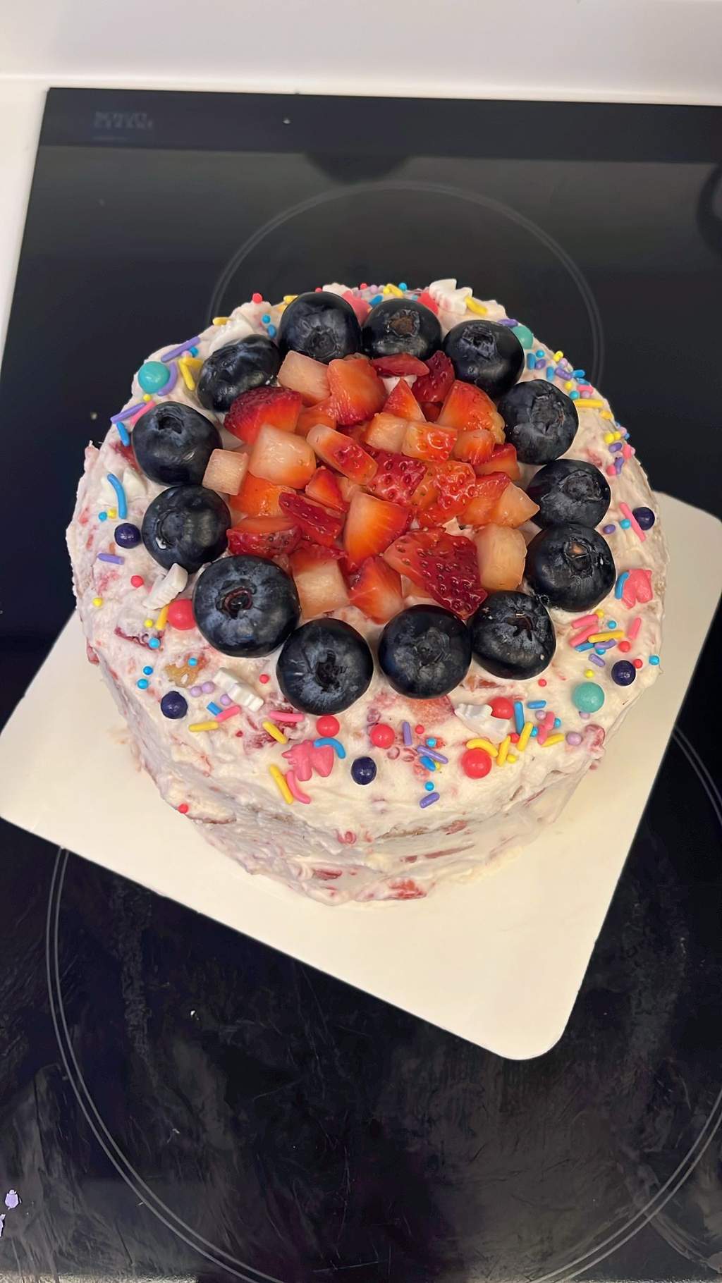 A birthday cake topped with fresh strawberries, blueberries and sprinkles, by Shirley.