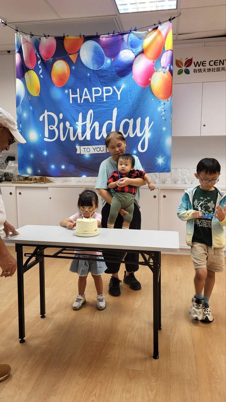 Two children stand beside a cake table and birthday backdrop.