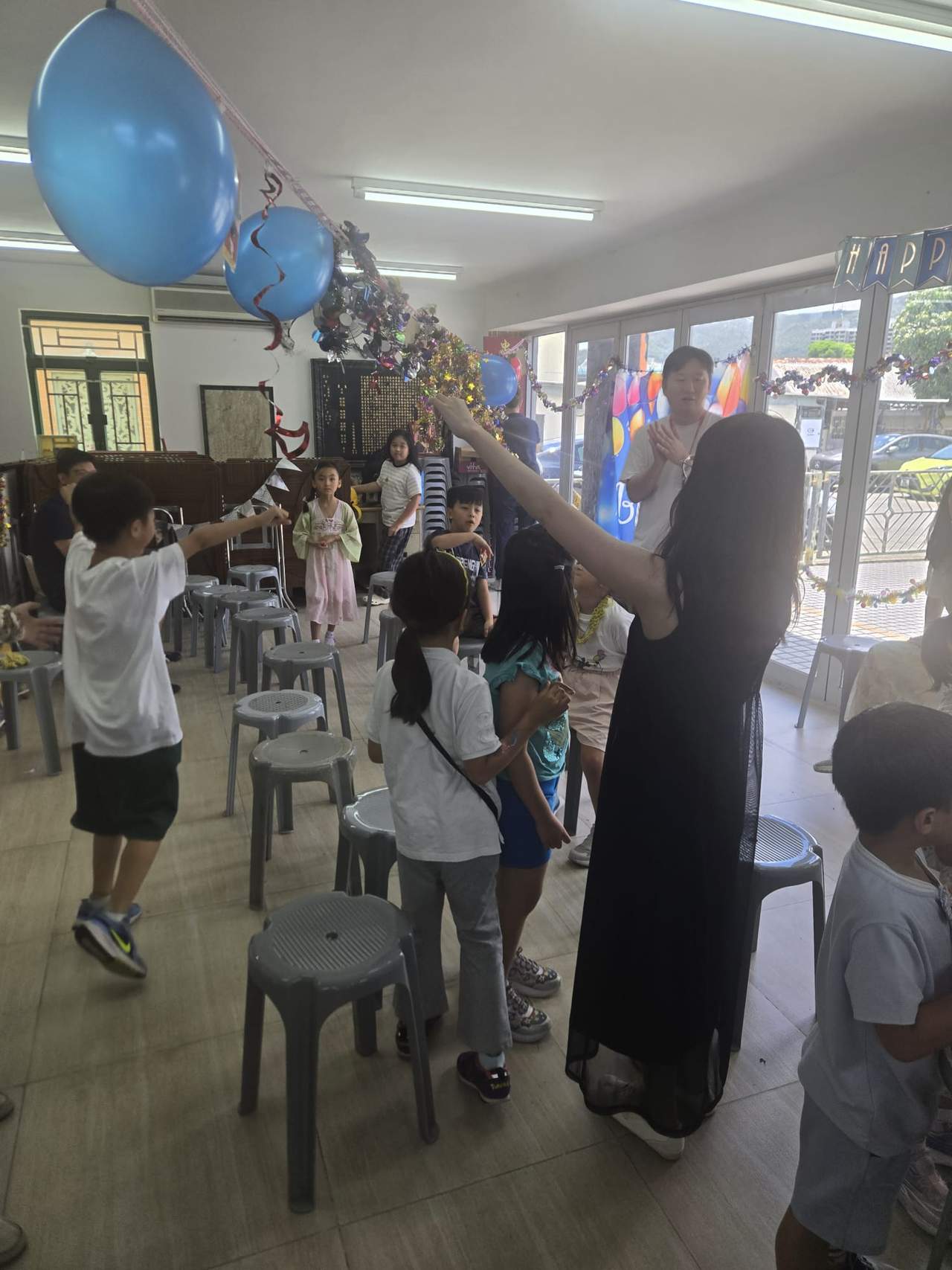 People stand among chairs and balloons during an indoor game.