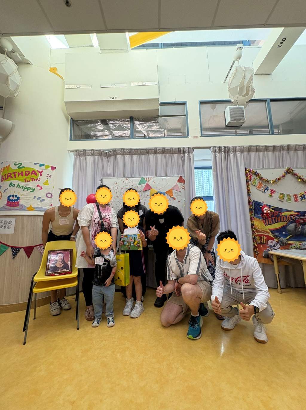 Children and volunteers posing together with gifts beneath birthday decorations.