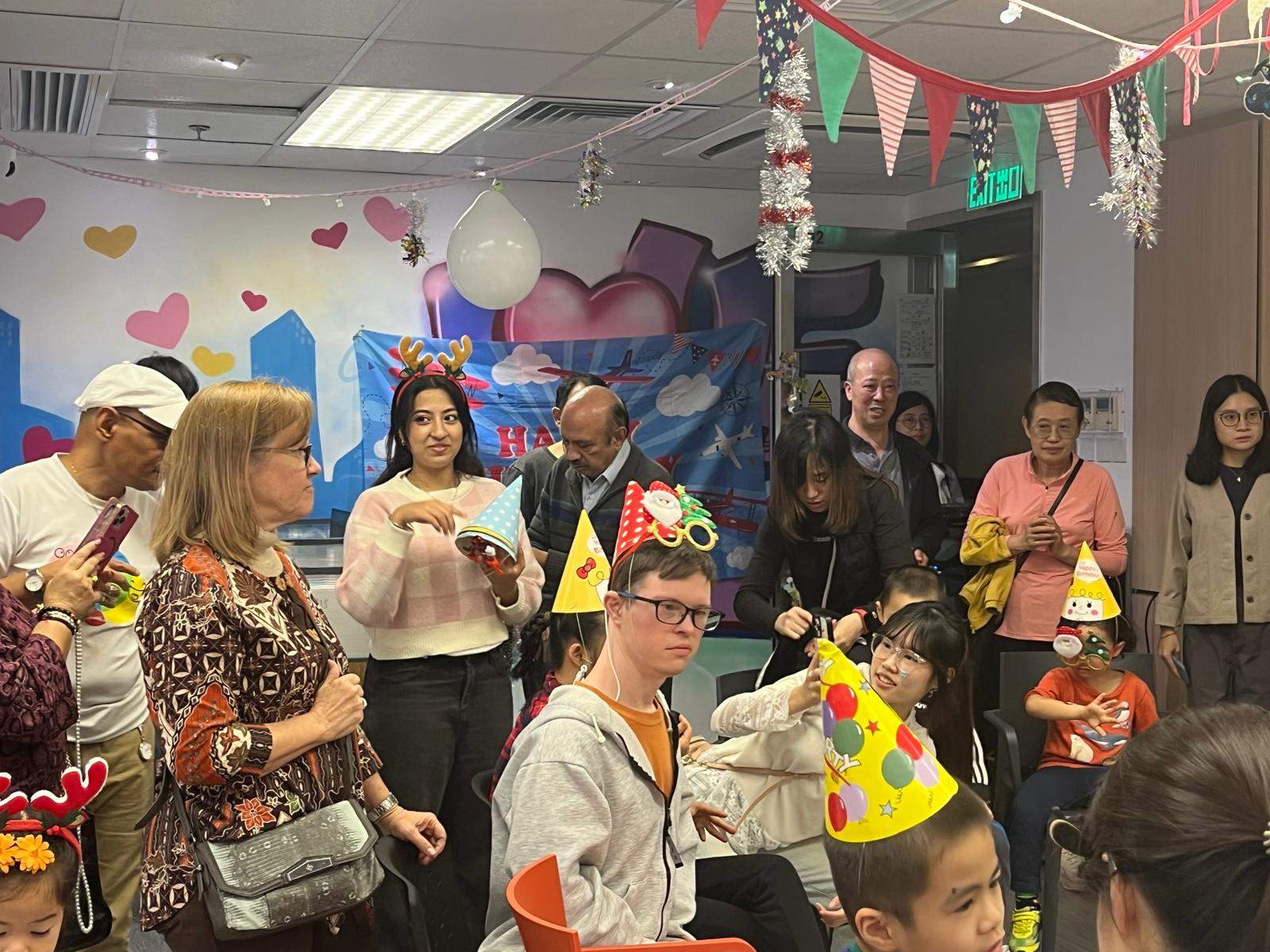 People in party hats gather near a decorated backdrop.