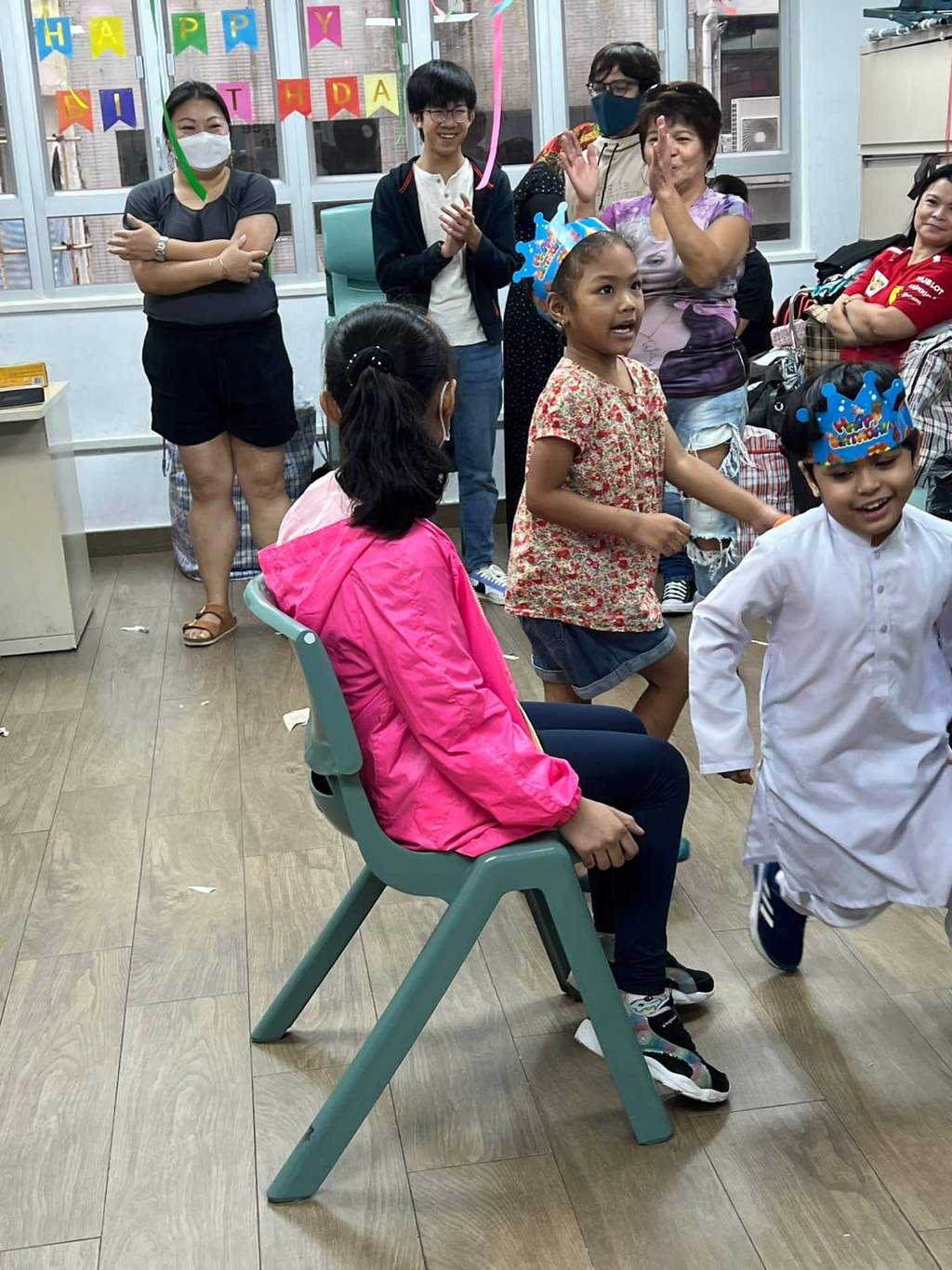 Children move around a chair while nearby adults watch the game.