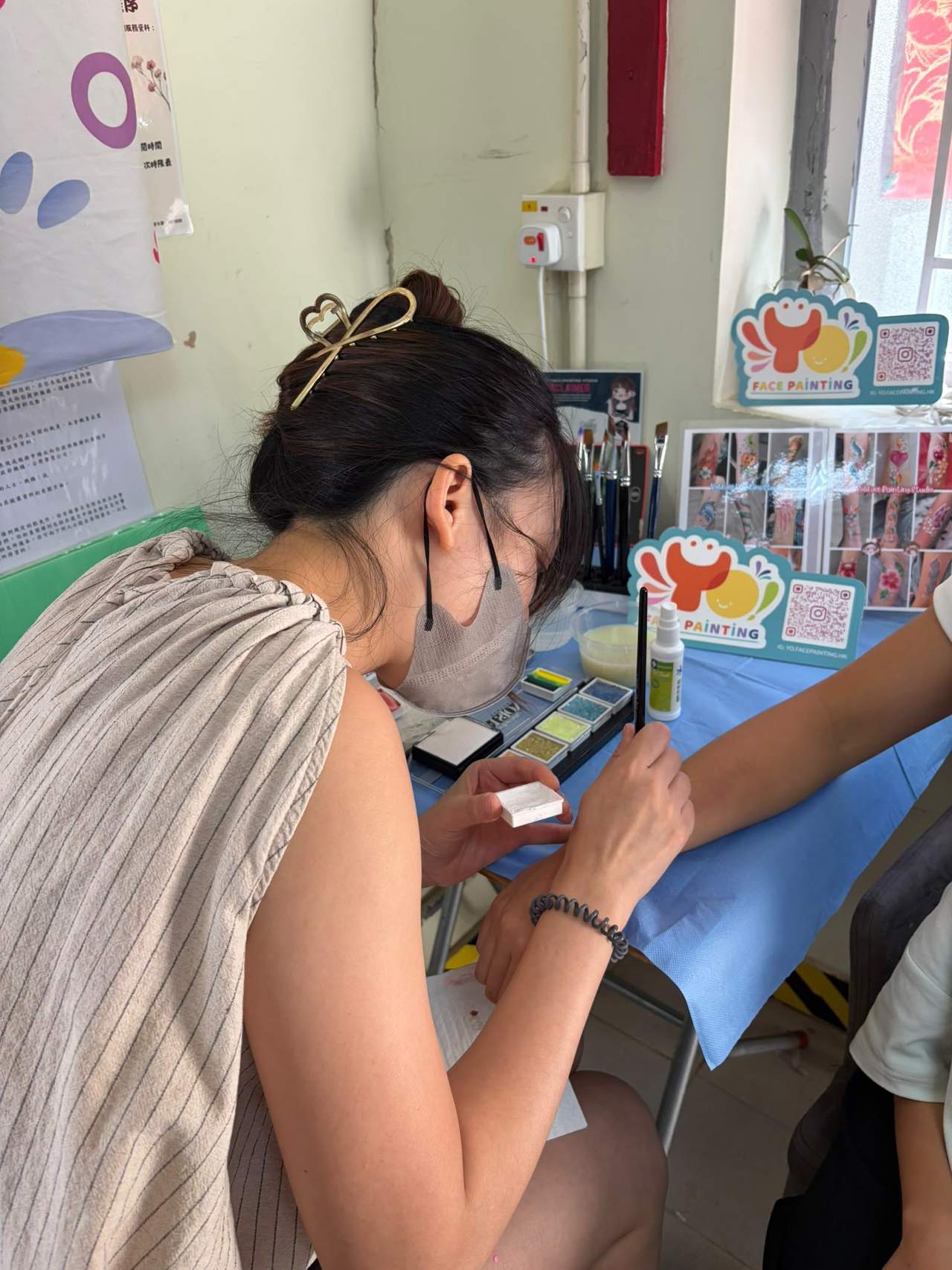 A face painter works at a table of colorful supplies.