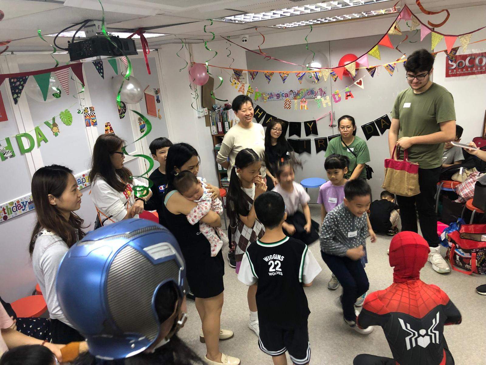 Adults and children gather around costumed performers near the backdrop.