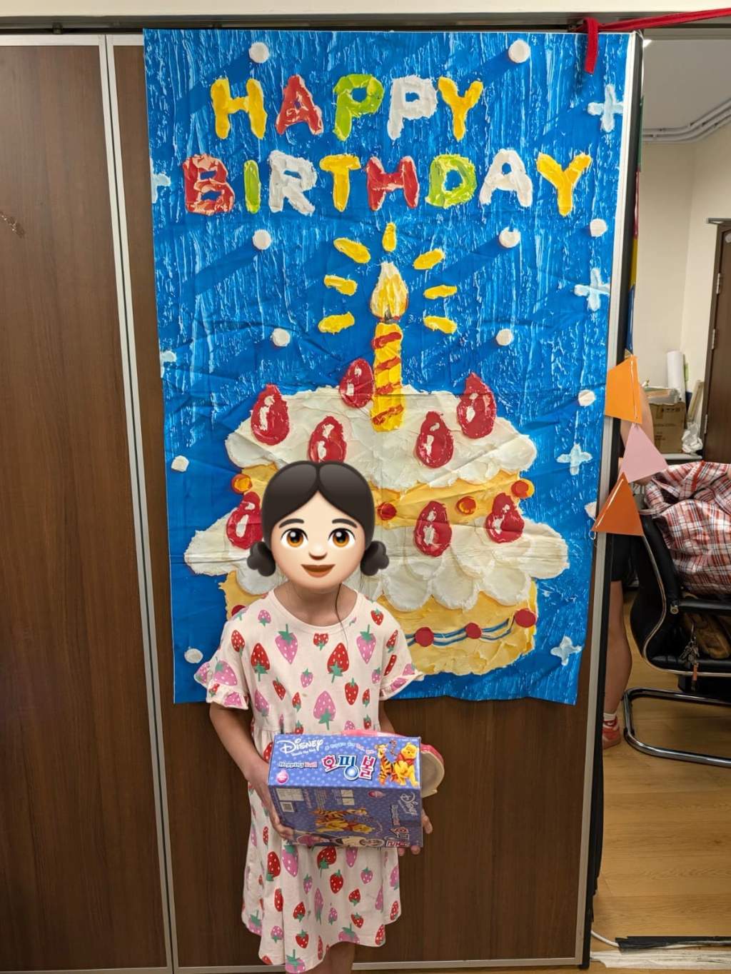 A child holds a boxed gift beside the birthday backdrop.