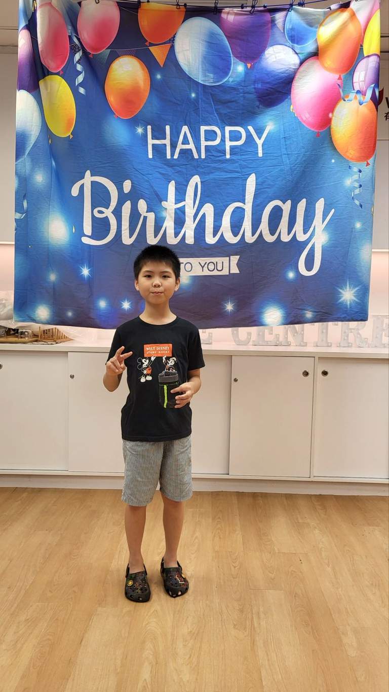 A child stands alone in front of the birthday backdrop.