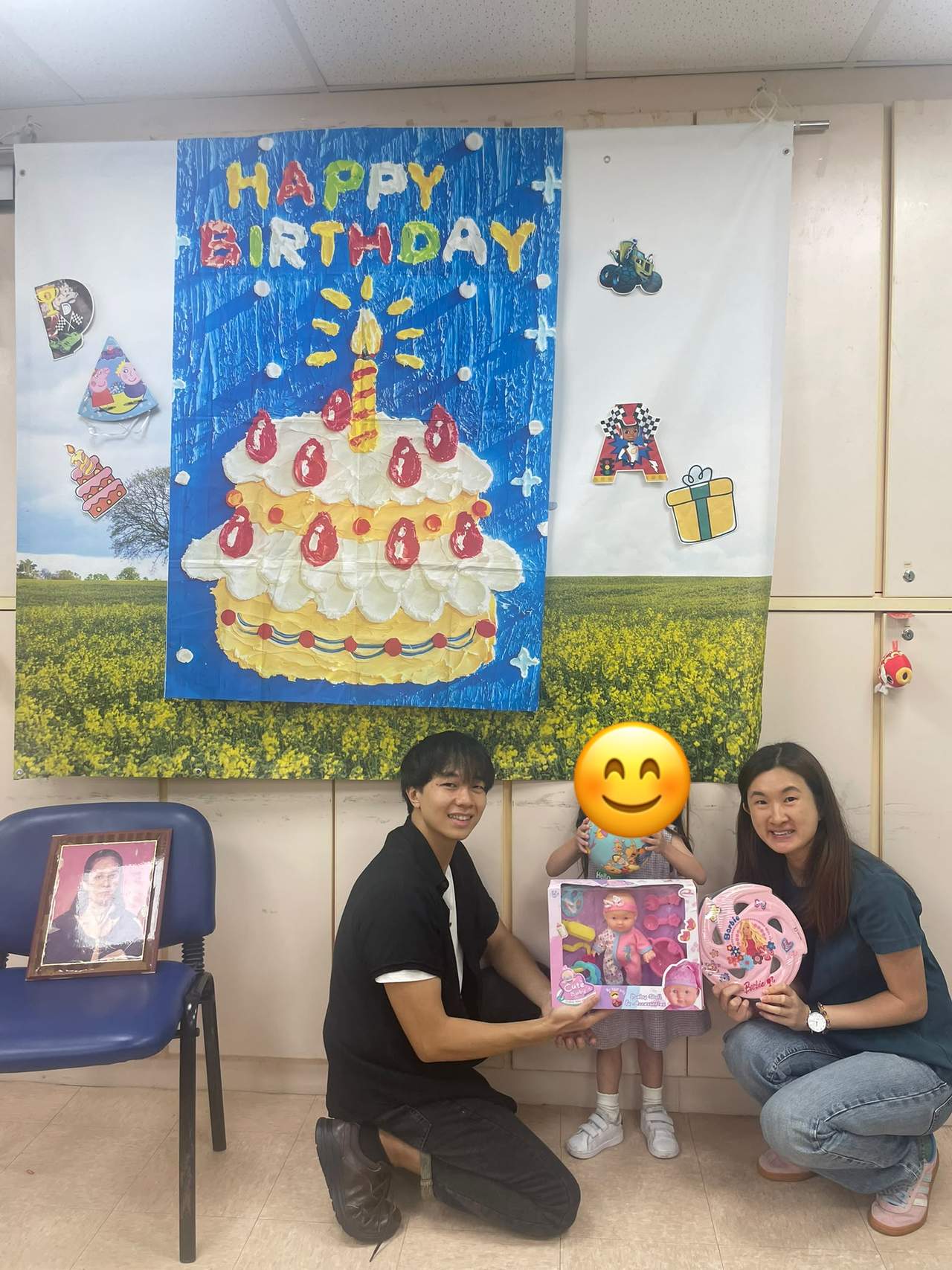 A child displays birthday gifts beside two adults.