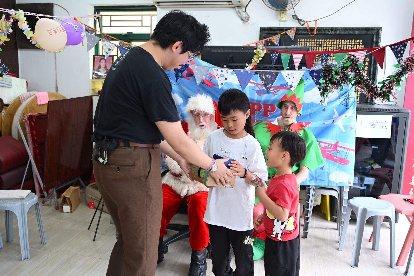 An adult guides two children during an activity near the backdrop.