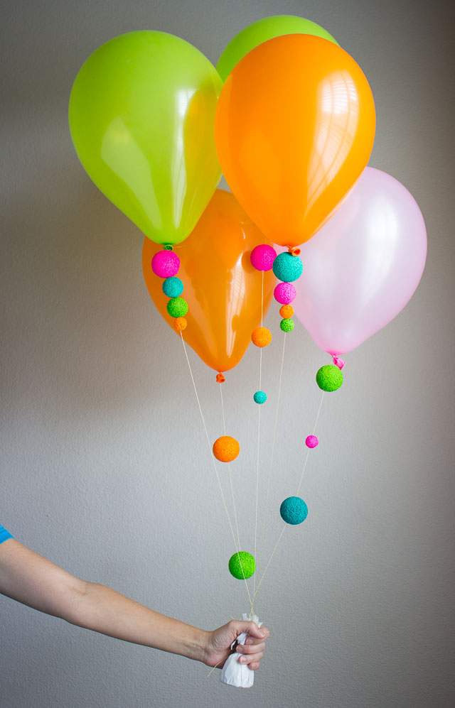 A hand holds strings attached to colourful floating balloons.