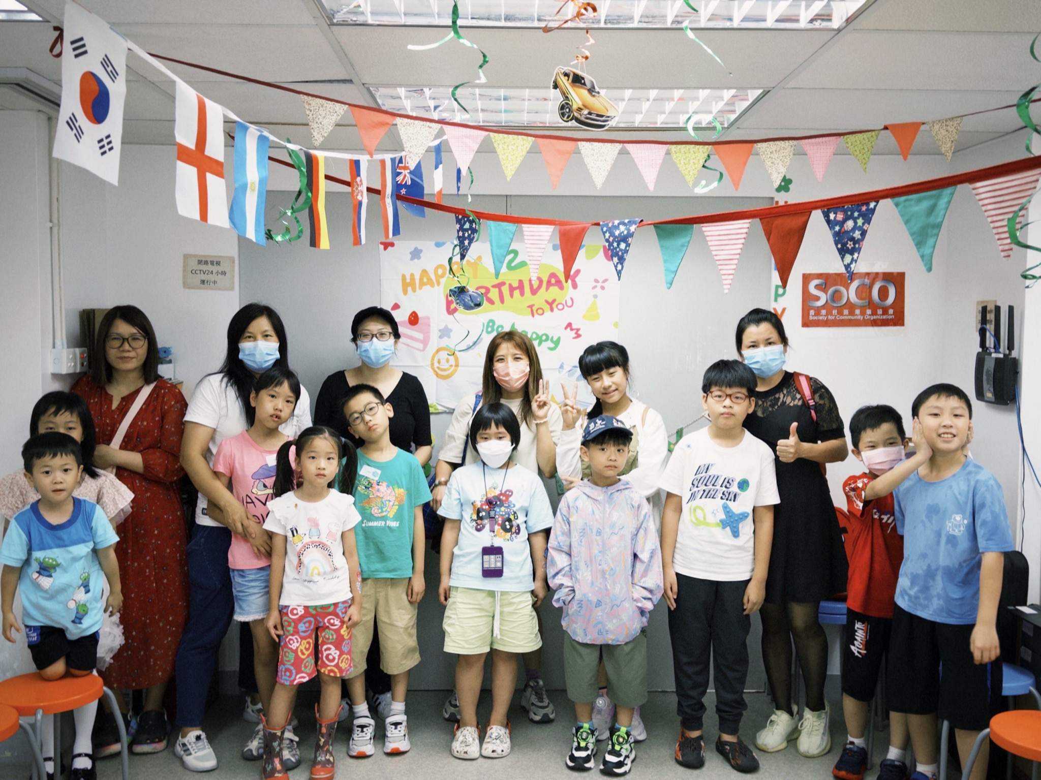 Adults and children pose together beneath international flags.
