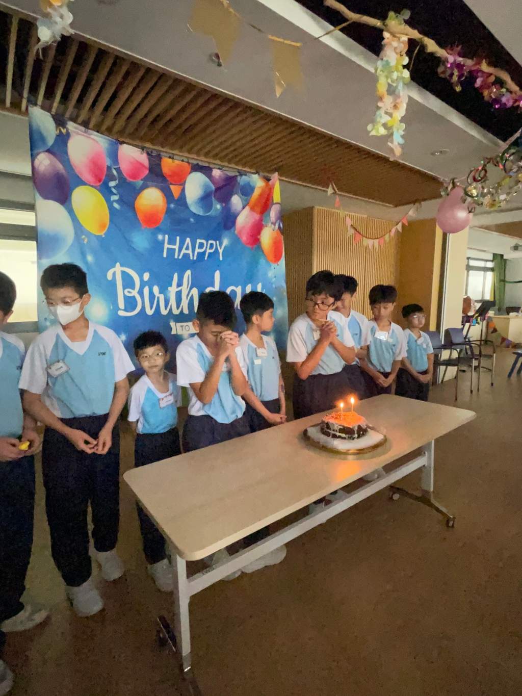 Children stand behind a lit cake on a table.