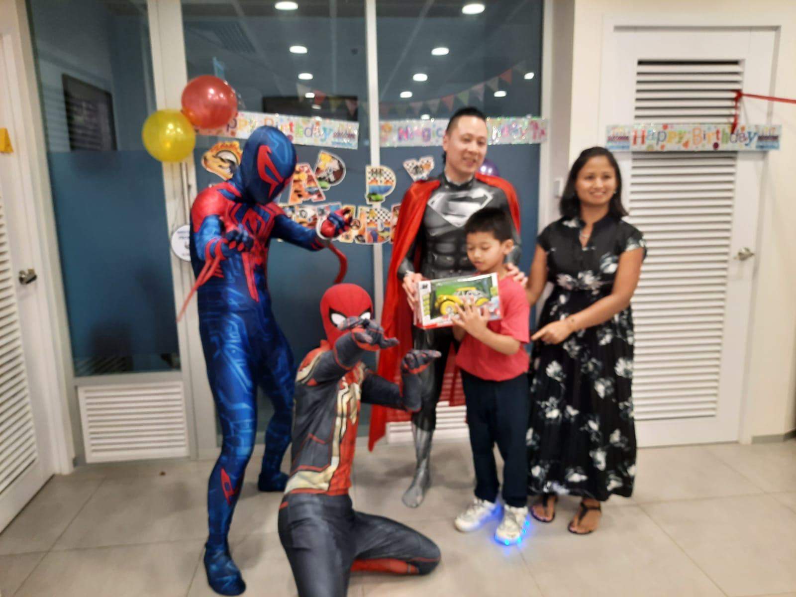 Costumed performers pose beside adults and a child holding a gift.