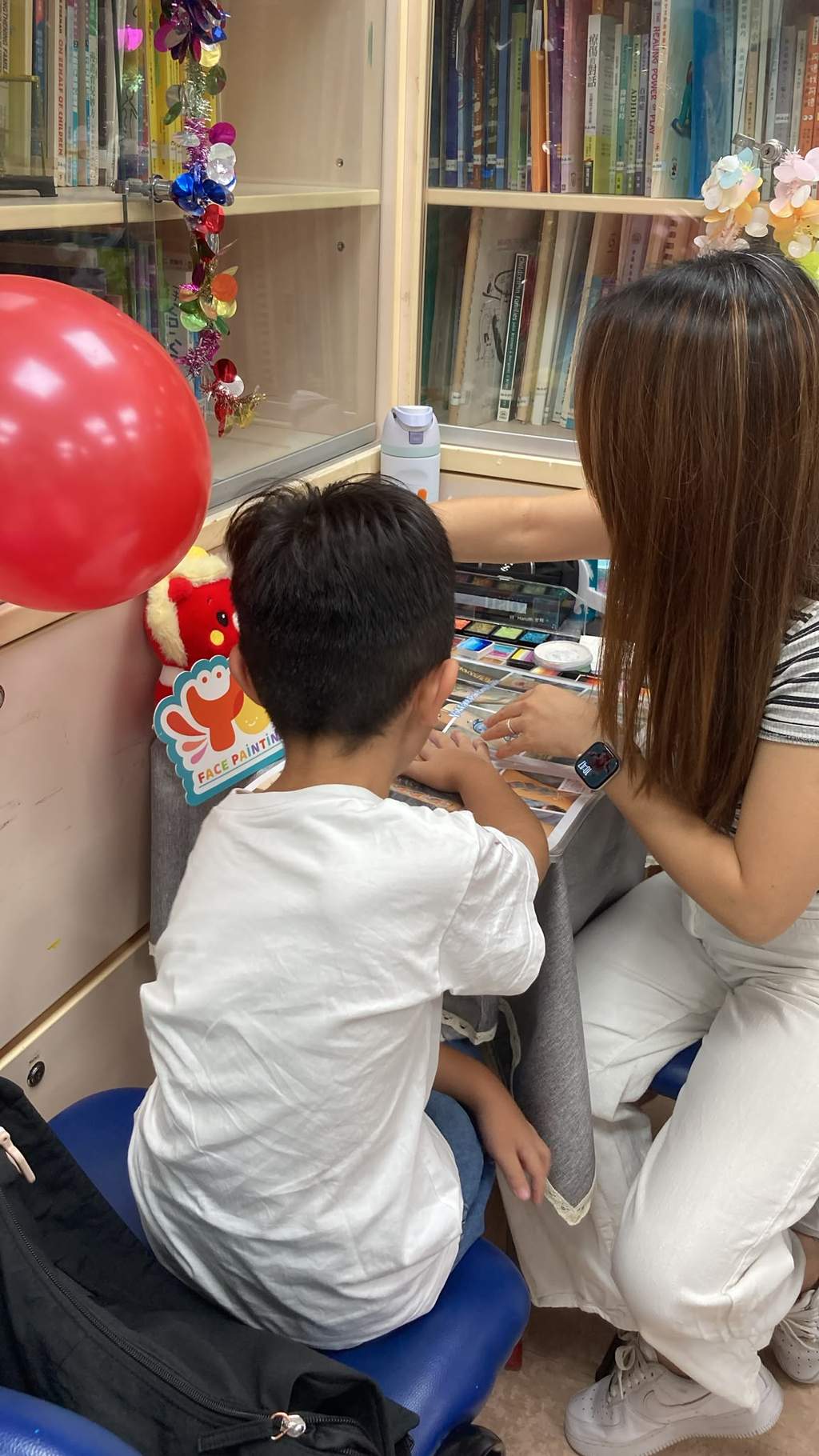 A child sits with an adult at a face-painting table.