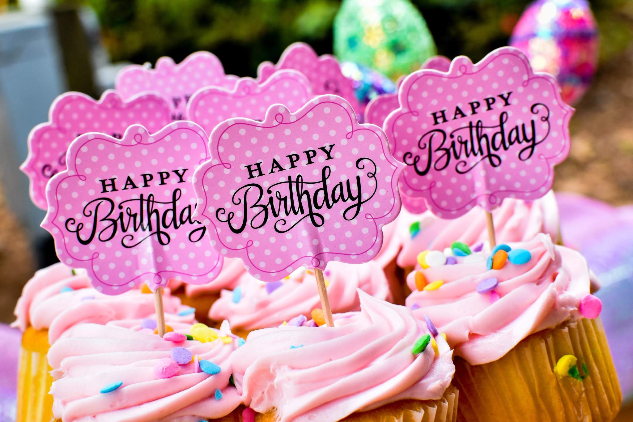 Pink-frosted cupcakes display decorative toppers and colourful sprinkles.
