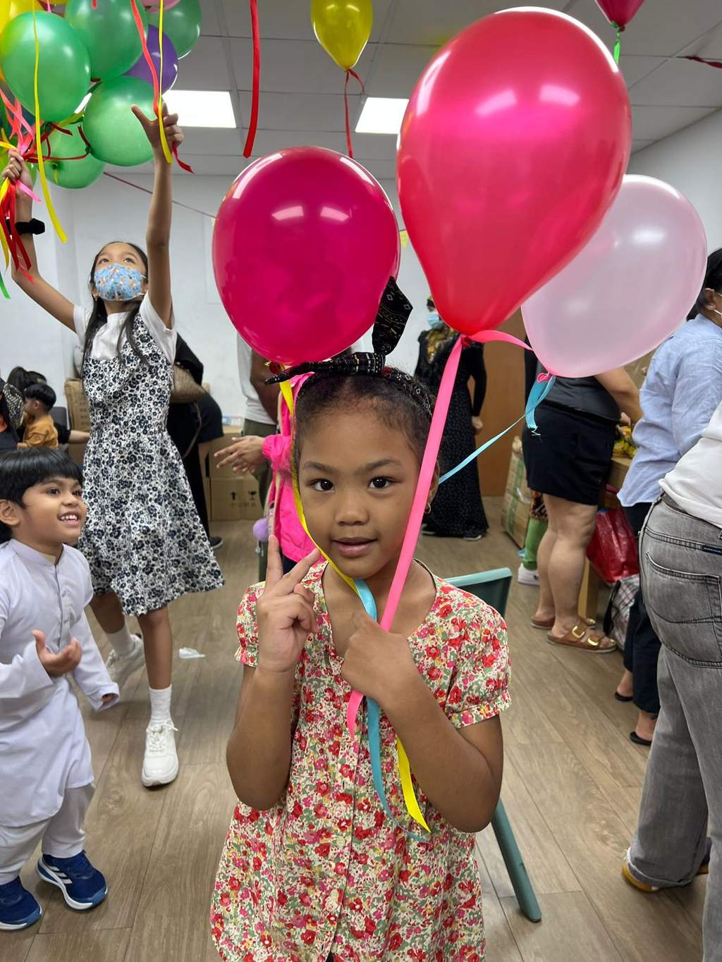 A child holds several balloon ribbons as people gather behind.