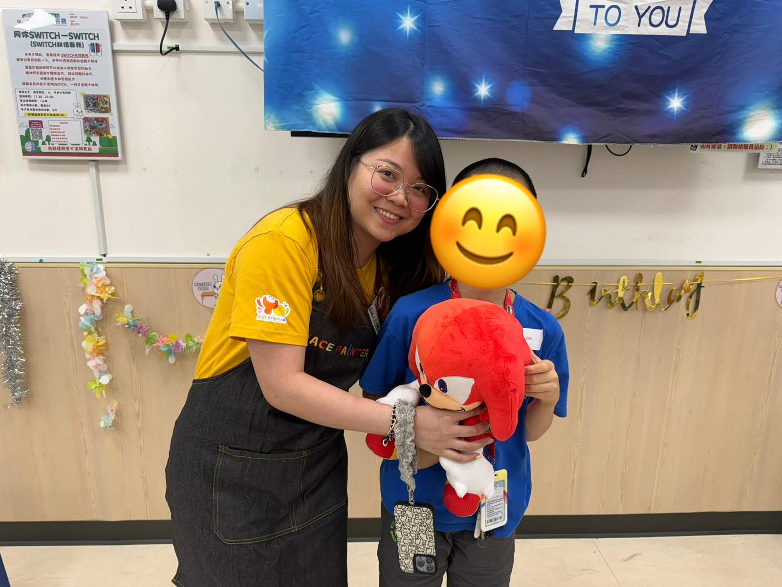 An adult poses with a child holding a stuffed toy.