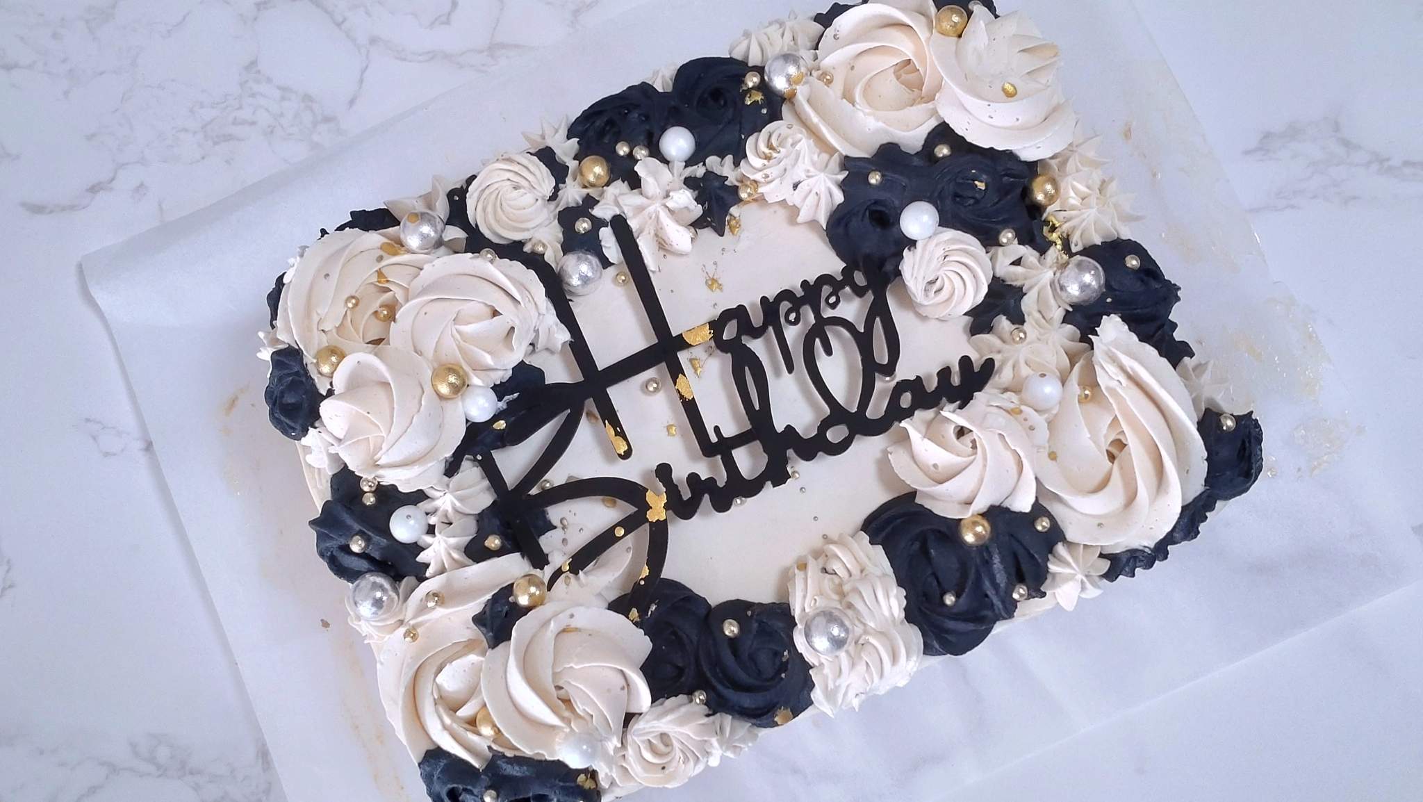 A black-and-white buttercream sheet cake with gold and silver pearls, by Bakelicious By Aisha.