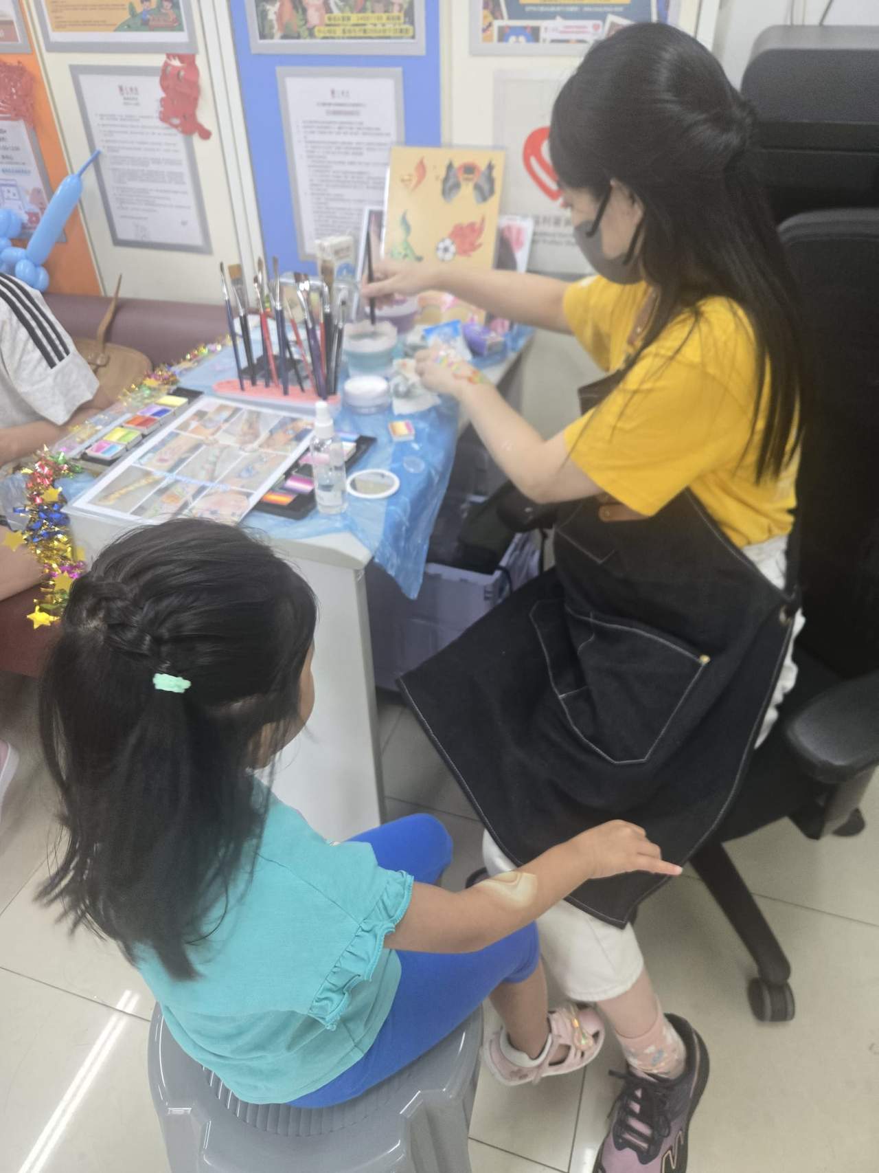 An adult applies face paint to a seated child.
