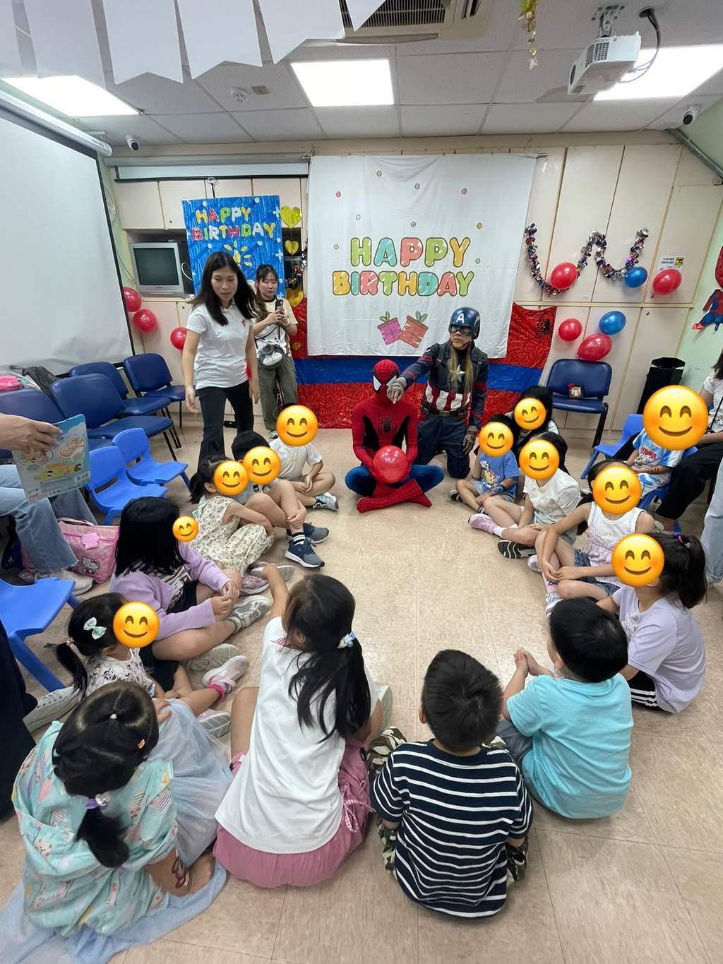 Children sit in a semicircle facing two costumed adults.