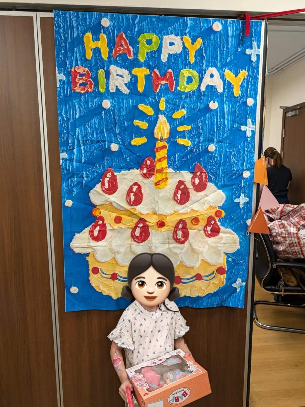 A child holds a boxed gift in front of the birthday backdrop.