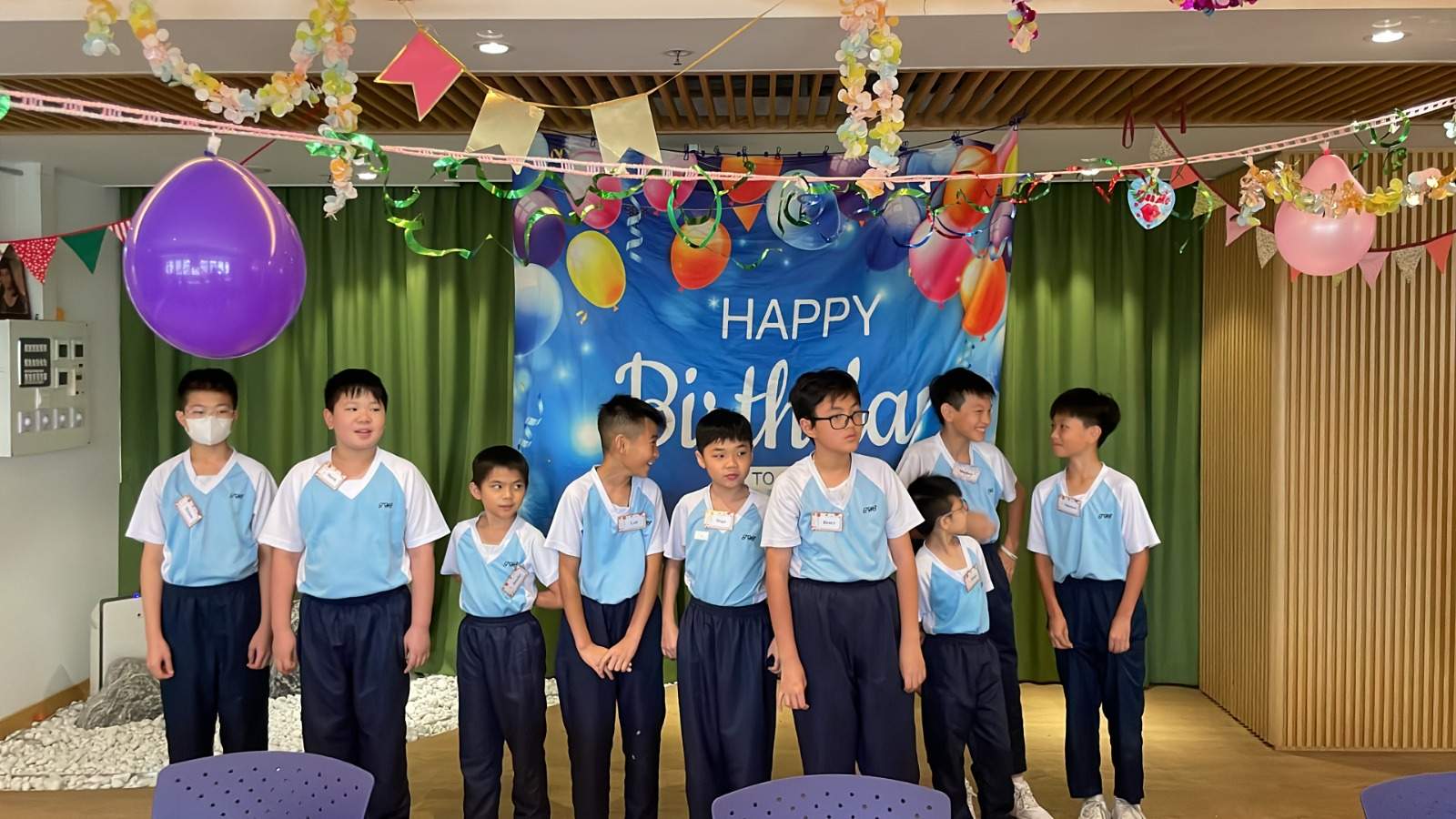 A row of children poses beneath balloons and birthday bunting.