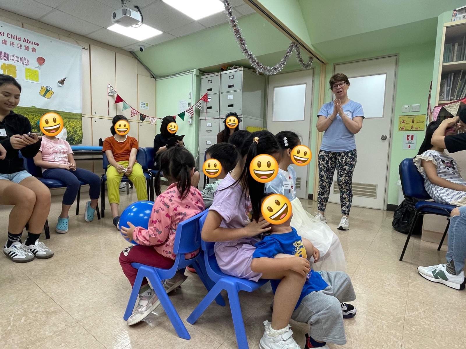 Children sit on small chairs while adults lead an activity.